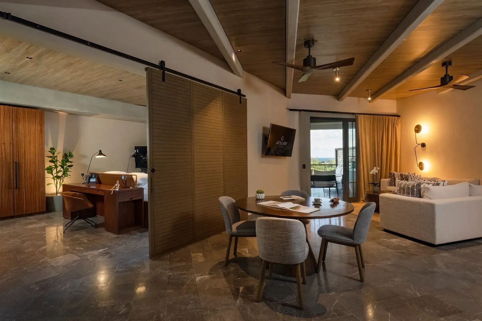 Offener Essbereich in der Suite mit rundem Holztisch, vier grauen Stühlen und Schiebetür.