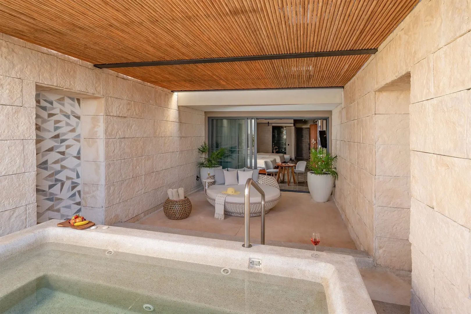 Überdachte Terrasse mit Whirlpool, Tagesbett und Natursteinwänden sowie Holzleistendecke.
