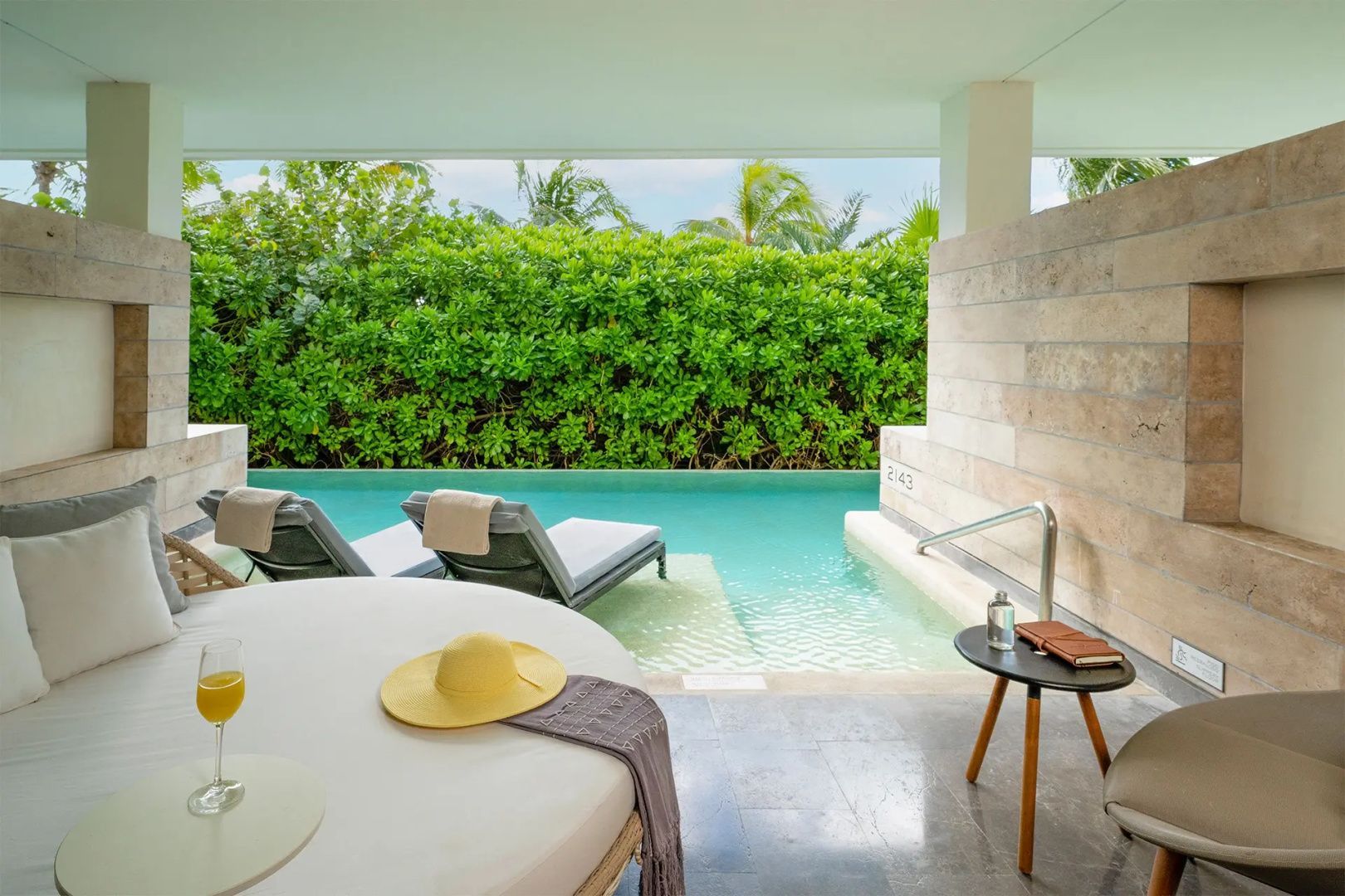Überdachte Terrasse mit Tagesbett und Blick auf einen Swim-Up-Pool mit Hecke.