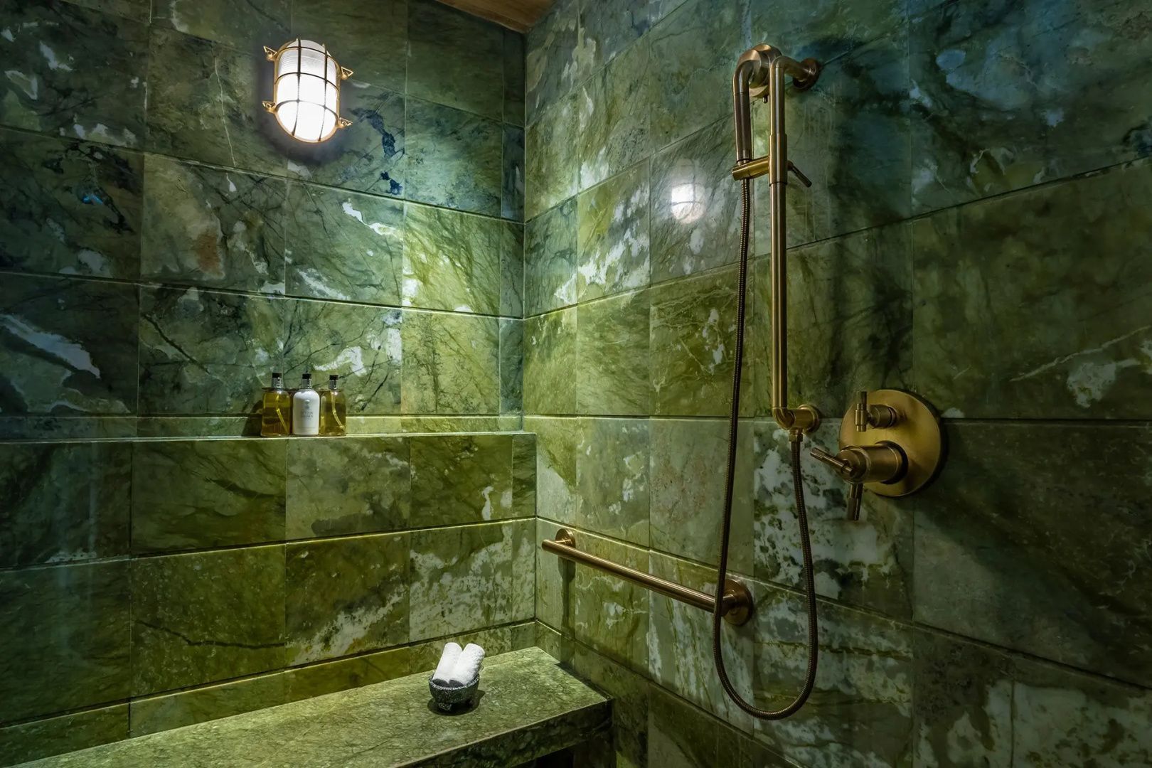 Duschbereich mit grünen Natursteinfliesen und goldenen Duscharmaturen.