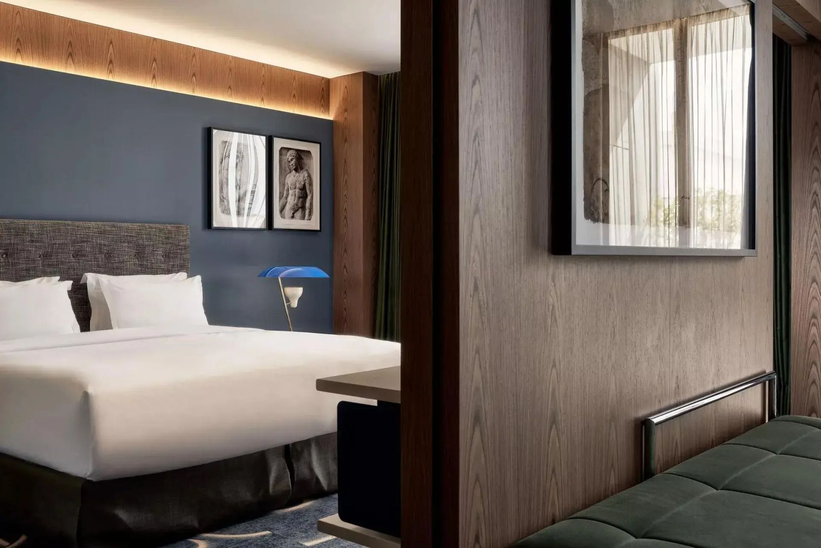 Blick in ein Schlafzimmer mit weiß bezogenem Doppelbett, blauer Wand und Holzverkleidung.