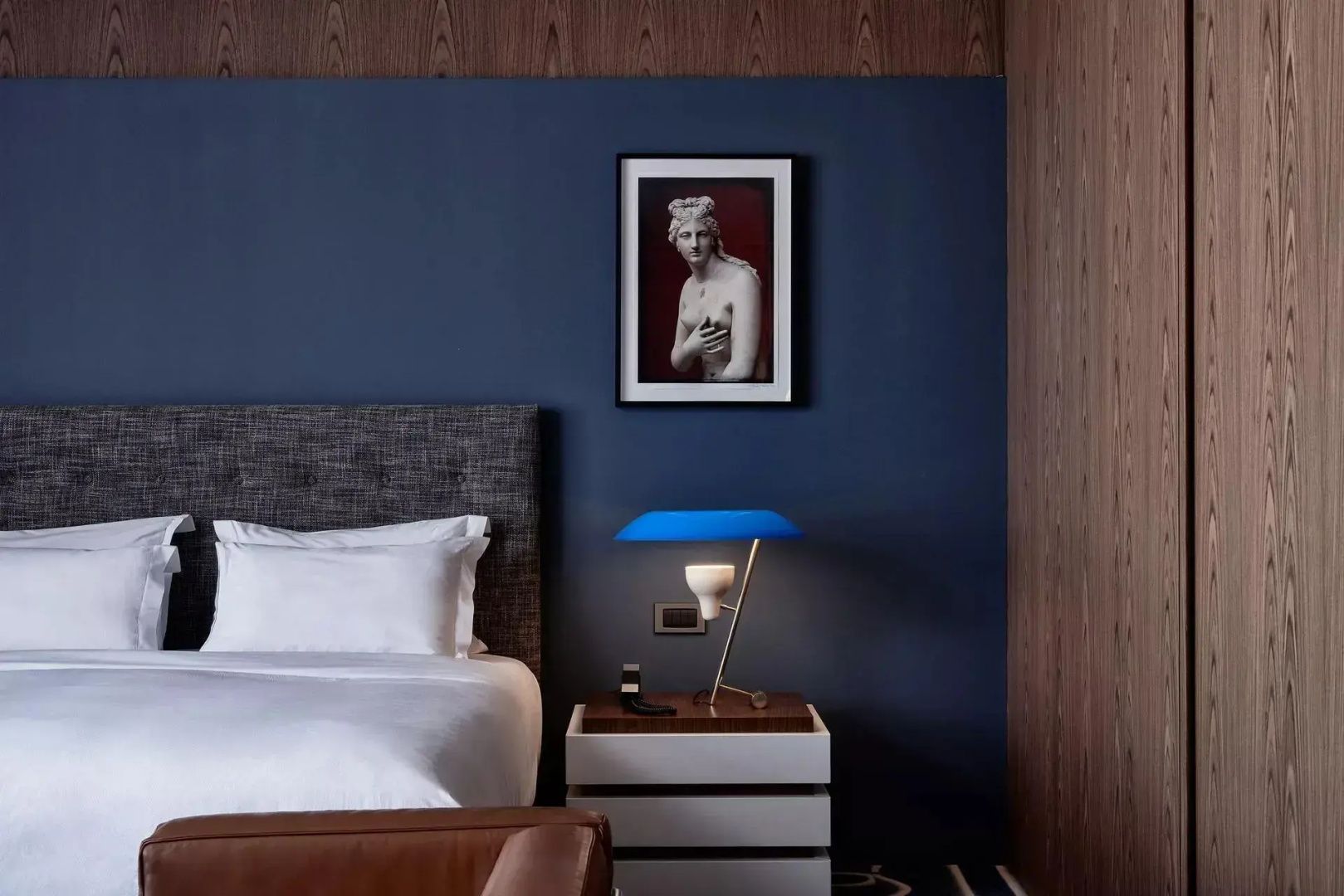 Schlafbereich mit einem Bett, blauer Wand, Nachttisch und einer blauen Tischleuchte.