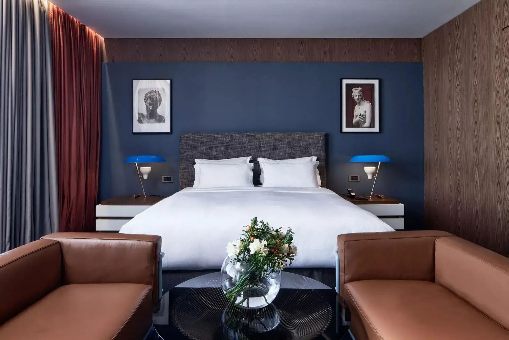Doppelbett mit weißer Bettwäsche vor blauer Wand mit blauen Nachttischlampen.
