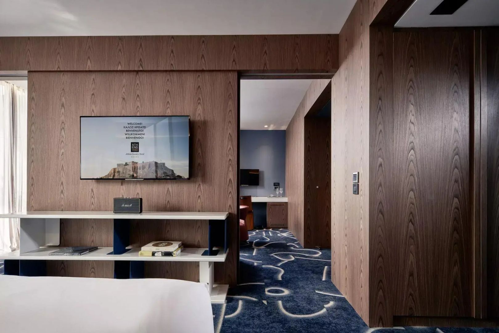 Wohnbereich mit holzverkleideter Wand, Flachbildfernseher und blau gemustertem Teppichboden.