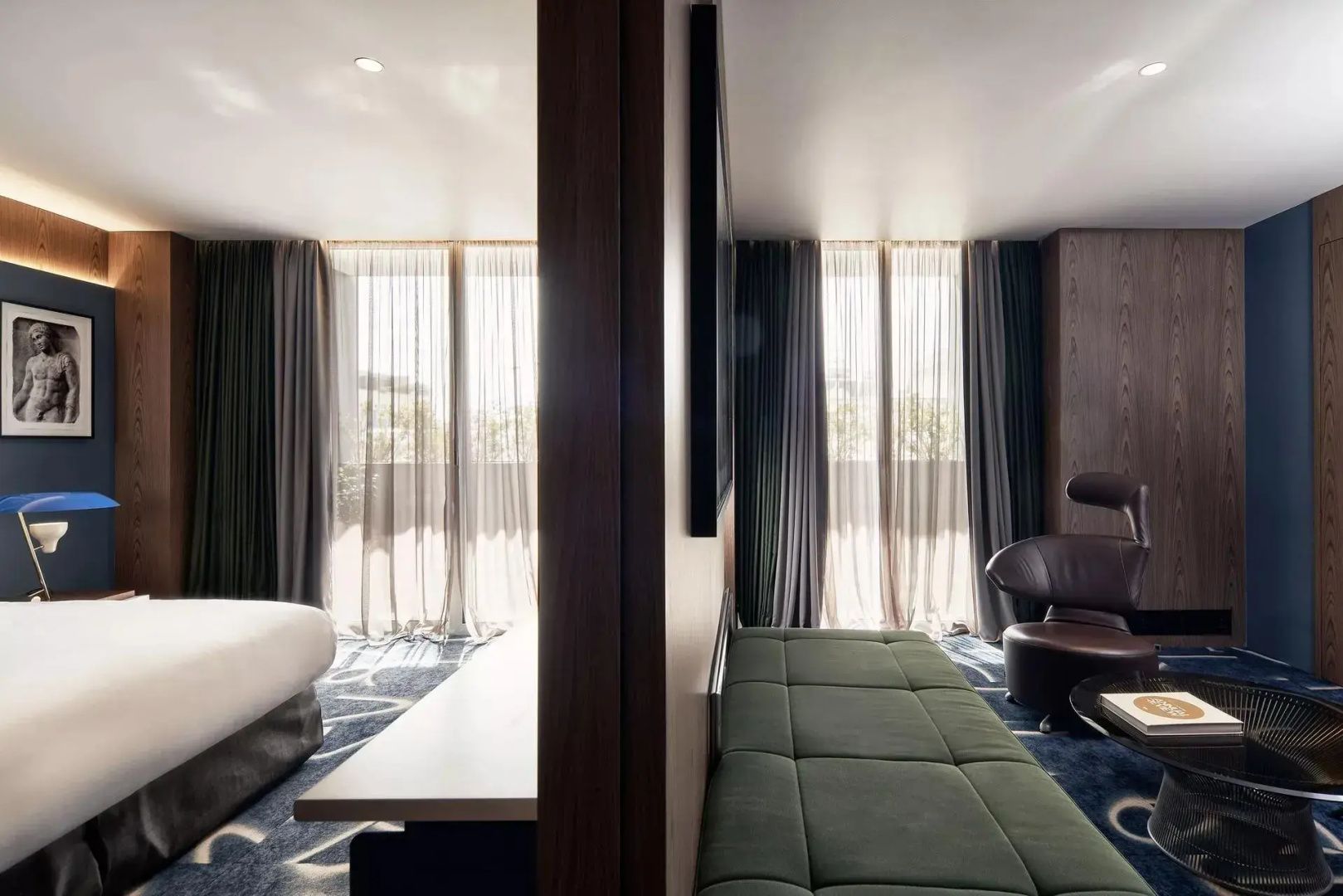 Sitzbereich im Hotelzimmer mit grüner Liege, Ledersessel und bodentiefen Fenstern.