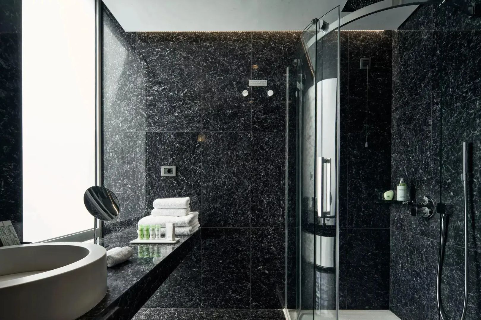 Badezimmerbereich mit Glasdusche, dunklen Natursteinwänden und Handtüchern.