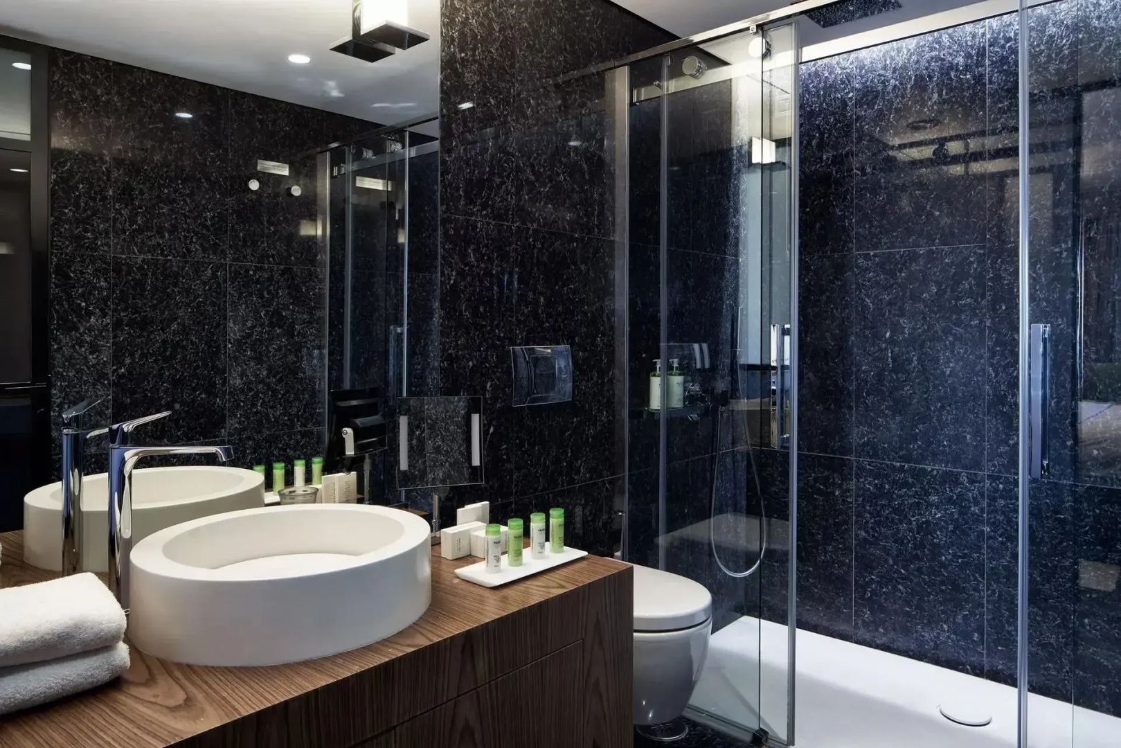 Badezimmer mit schwarzer Wandverkleidung, Dusche, Toilette und weißem Waschtisch.