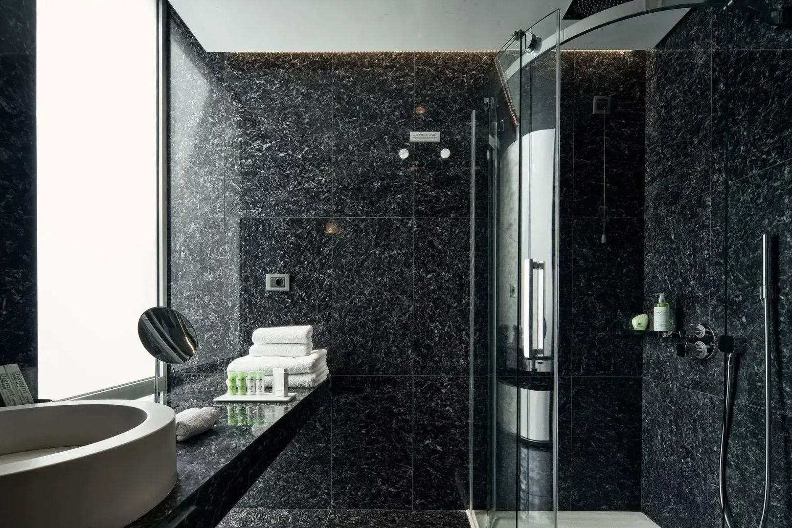 Badezimmer mit Glasduschkabine, dunkler Steinwand und Waschtisch