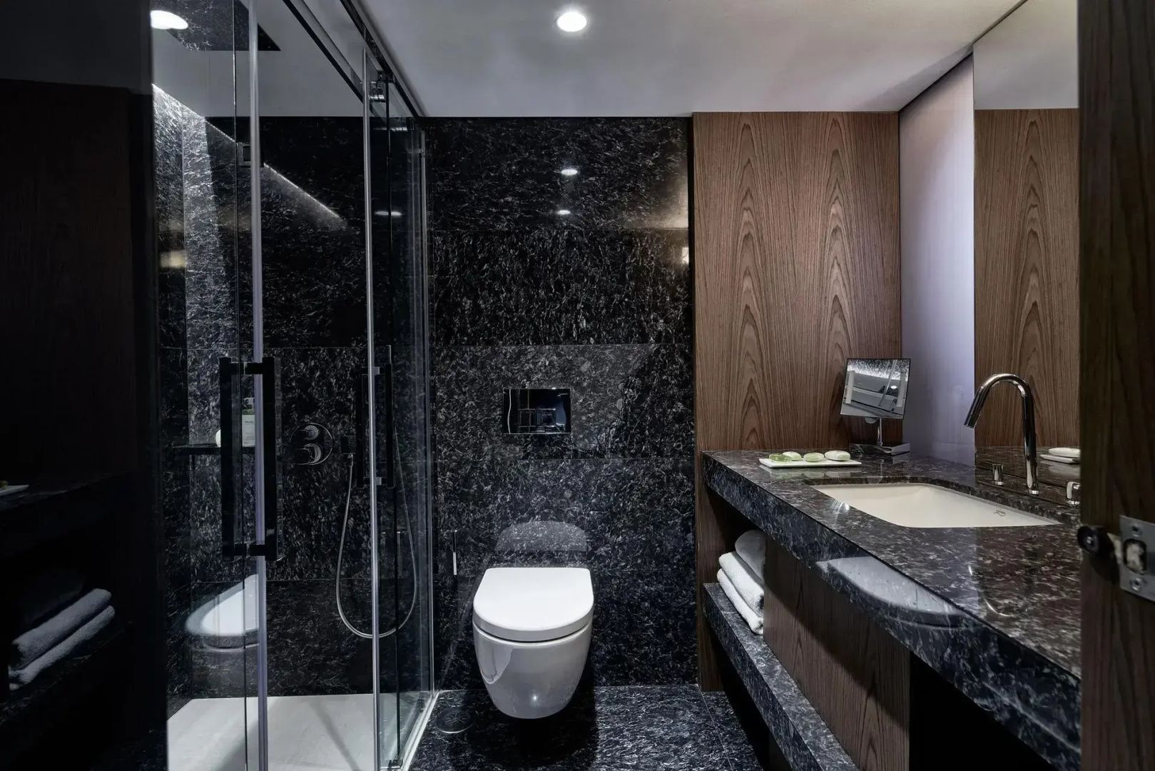Badezimmer mit gläserner Duschkabine, Toilette und dunklen Marmorfliesen.