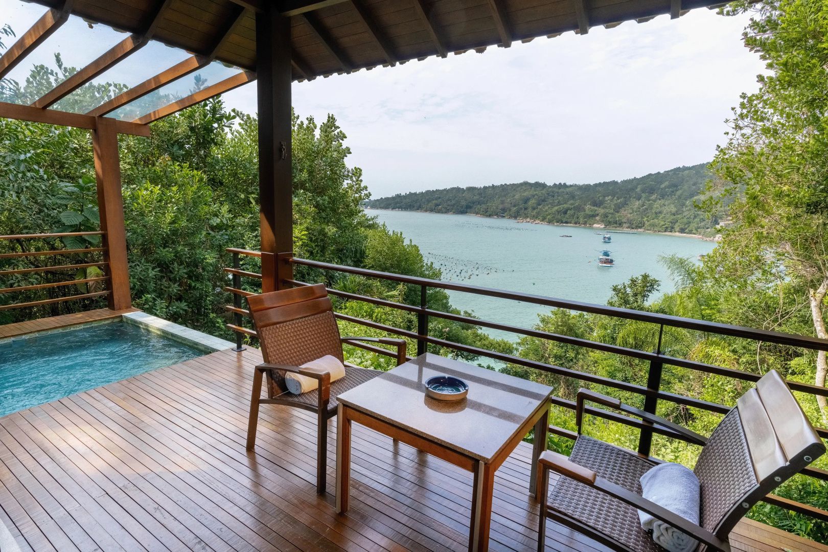 Holzveranda mit Tisch und Stühlen sowie Weitblick auf eine grüne Küstenlandschaft und das Meer.