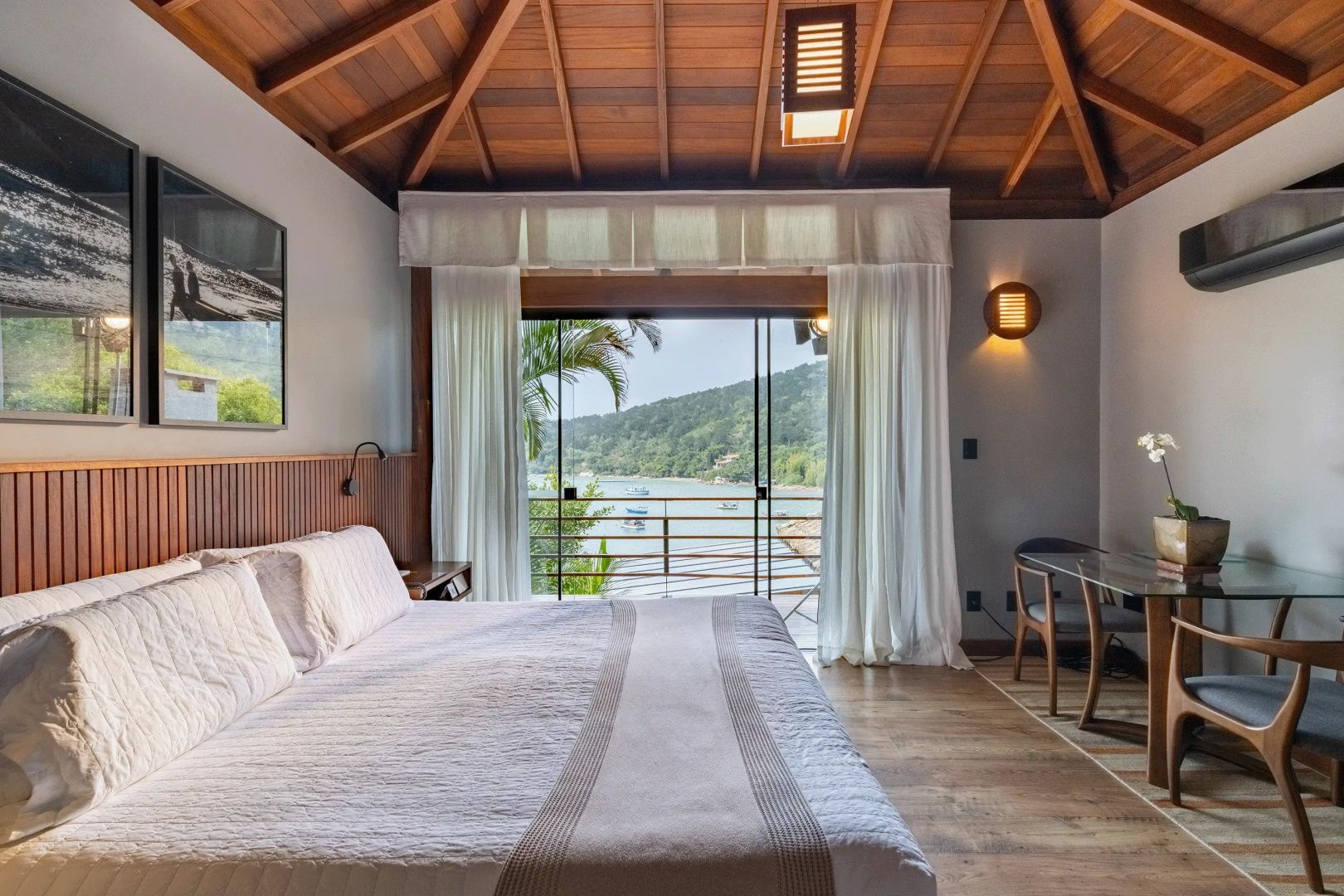 Doppelbett im Zimmer mit Holzboden und Blick durch die Glasfront auf das Wasser.