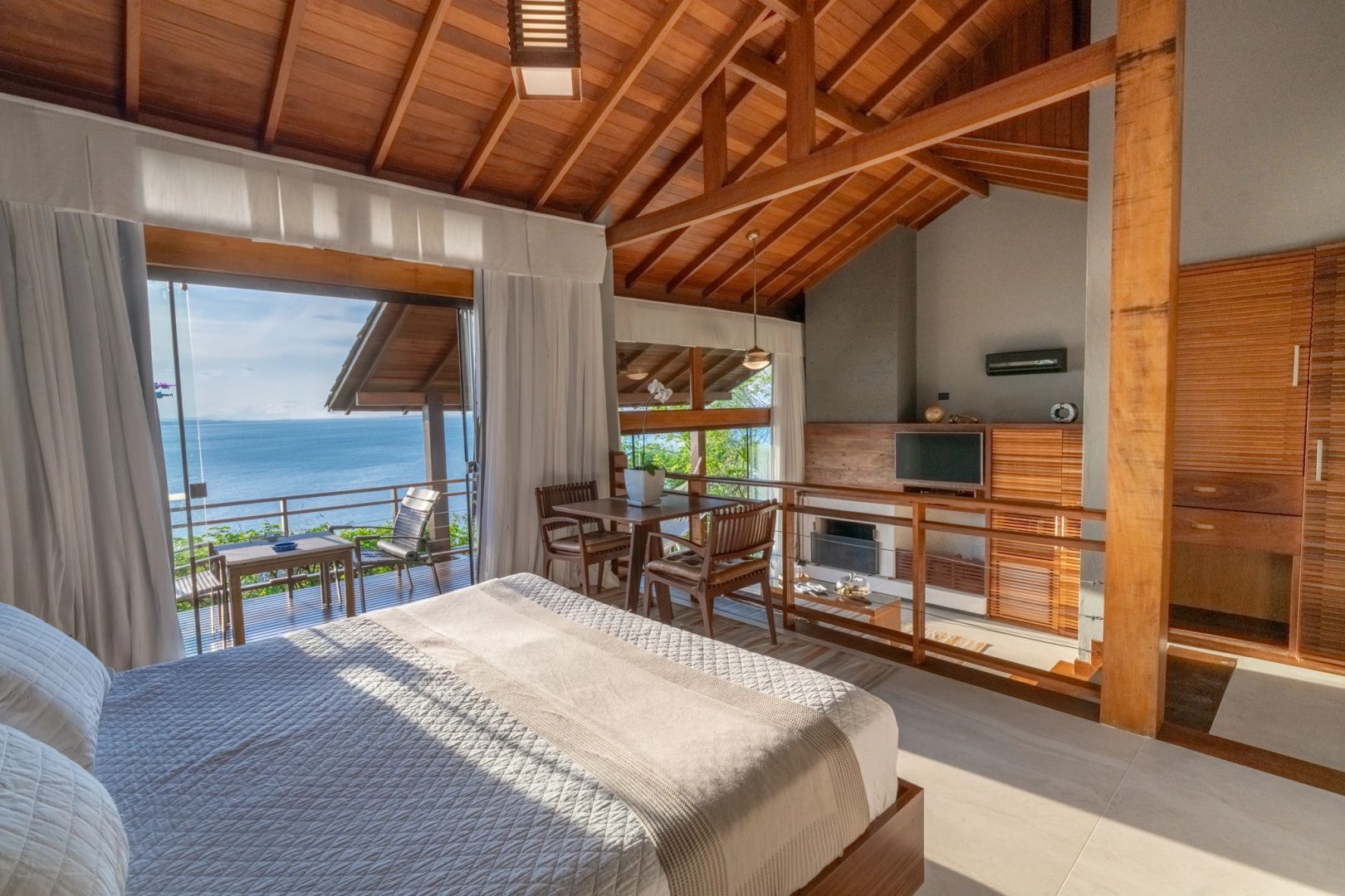 Schlafbereich einer Suite mit großem Bett, Holzdecke und Balkon mit Blick auf den Ozean.