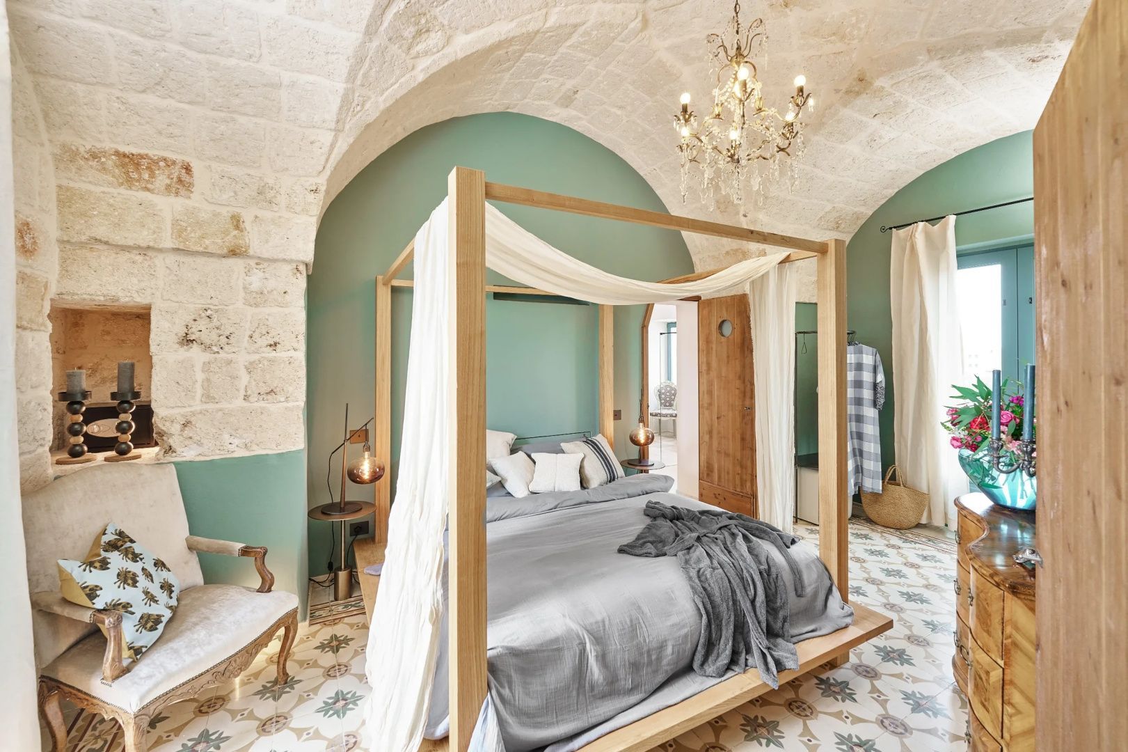 Helles Schlafzimmer mit einem hölzernen Himmelbett, Kissen, Kreuzgewölbe und Kronleuchter.
