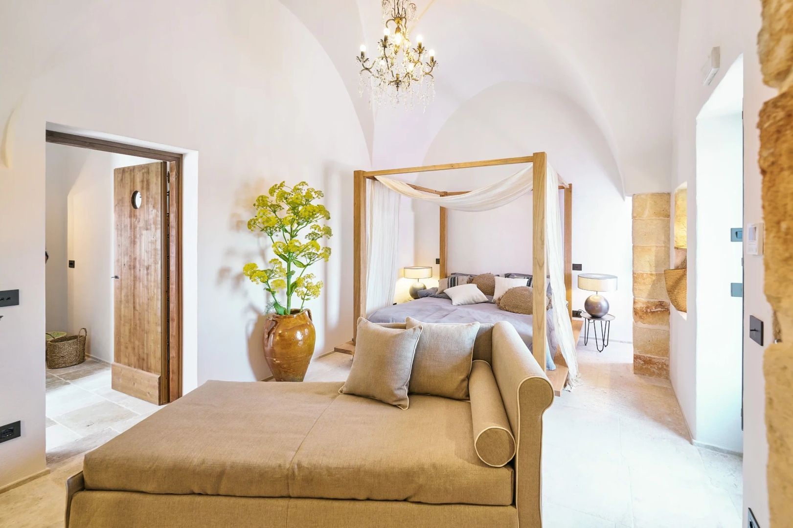 Helles Schlafzimmer mit Gewölbedecke, Himmelbett aus Holz, Recamiere und Kronleuchter.