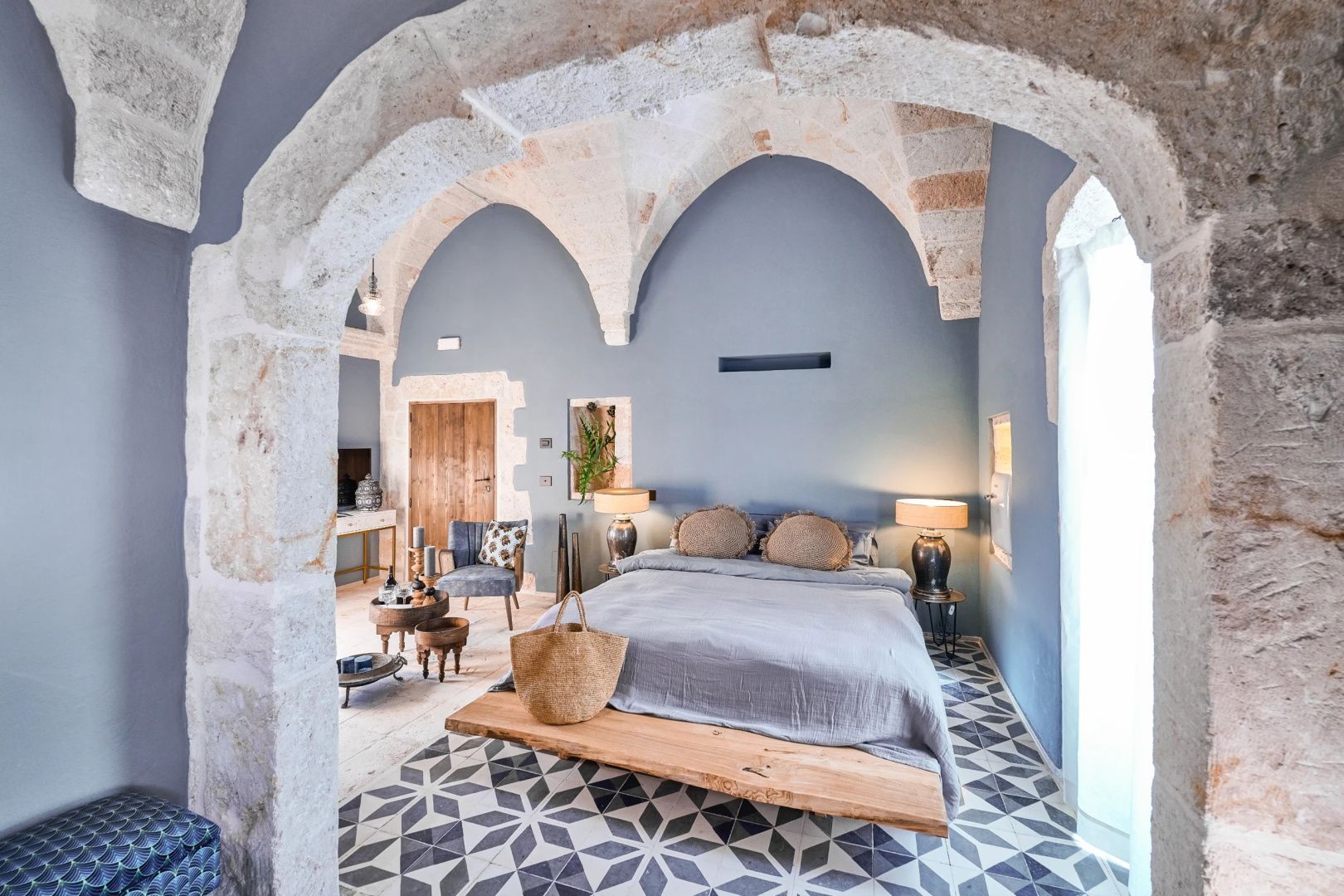 Schlafzimmer mit Steingewölbe, blau gestrichener Wand, Doppelbett und gemusterten Fliesen.