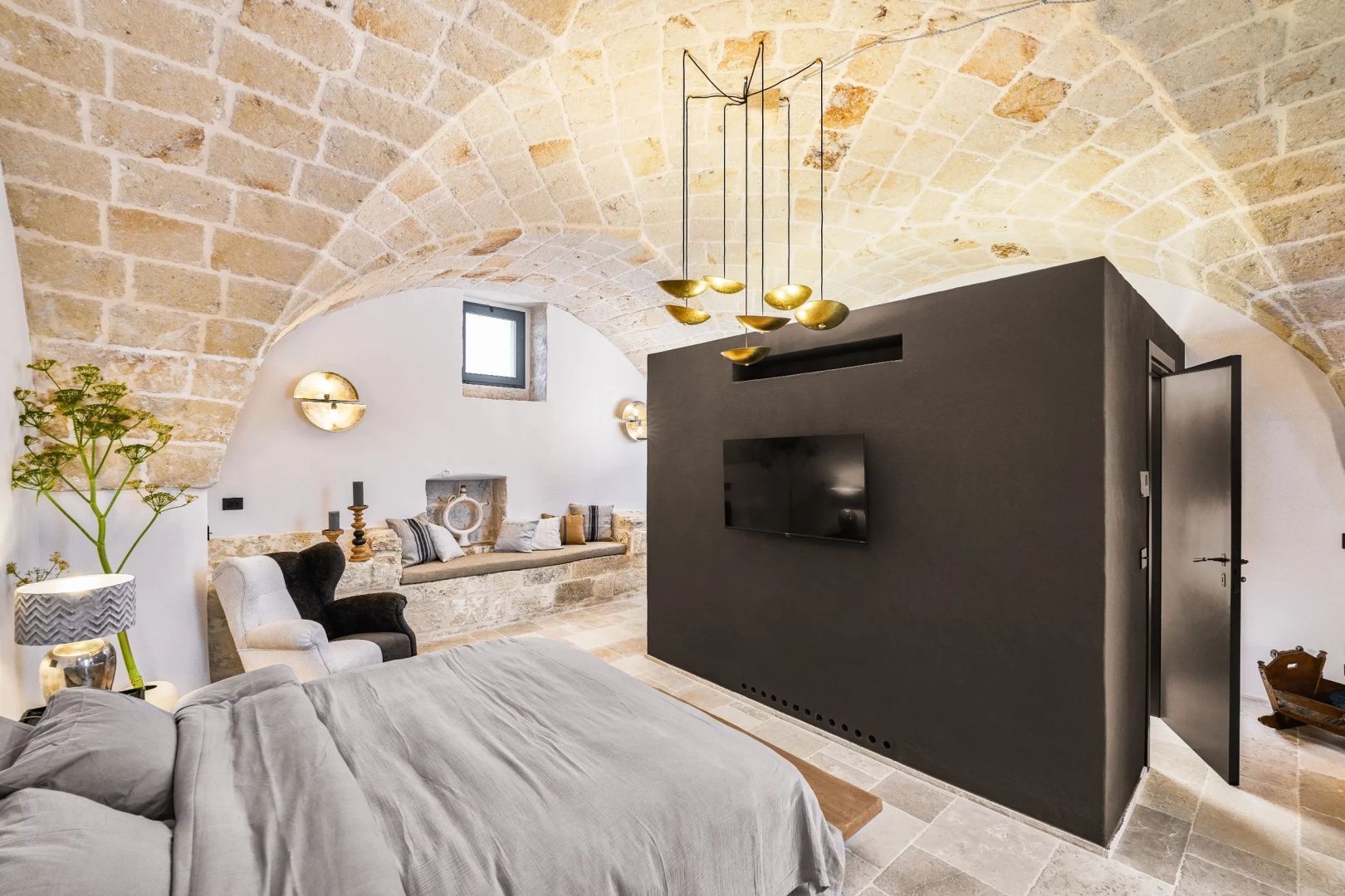 Schlafzimmer mit Natursteingewölbe, brauner Trennwand und Flachbildfernseher.