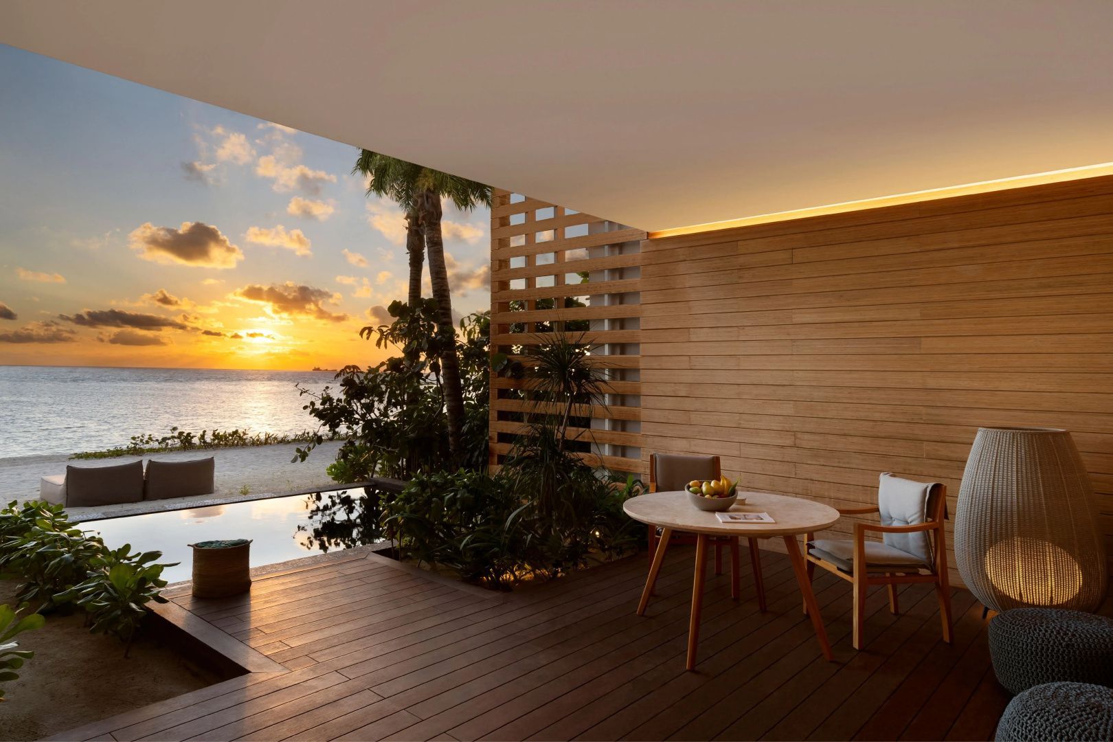 Überdachte Terrasse mit Holzdeck, Esstisch und Blick auf das Meer bei Sonnenuntergang.