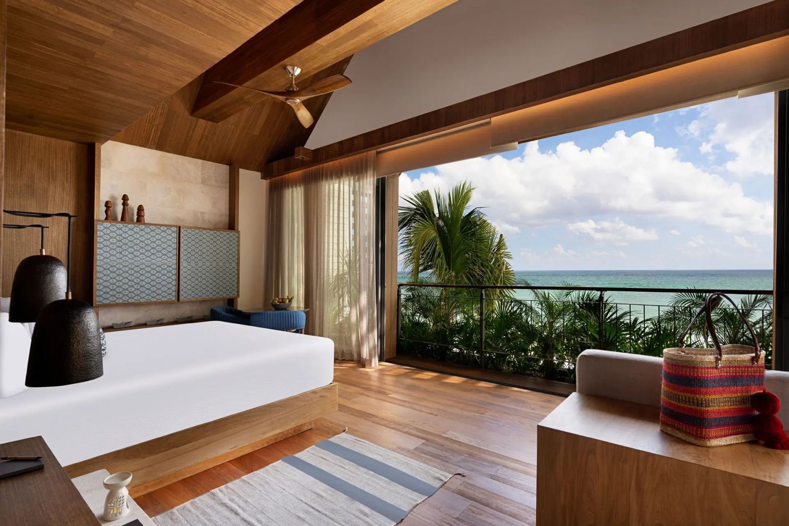 Schlafzimmer mit weißem Bett und geöffneter Glasfront zum Balkon mit Blick auf das Meer.