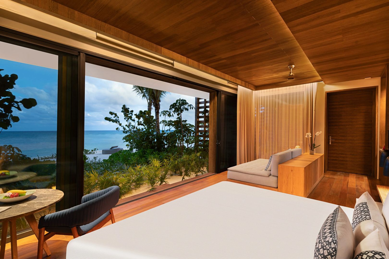 Moderne Suite mit Holzverkleidung, Sitzbereich und Blick durch die Glasfront aufs Meer.