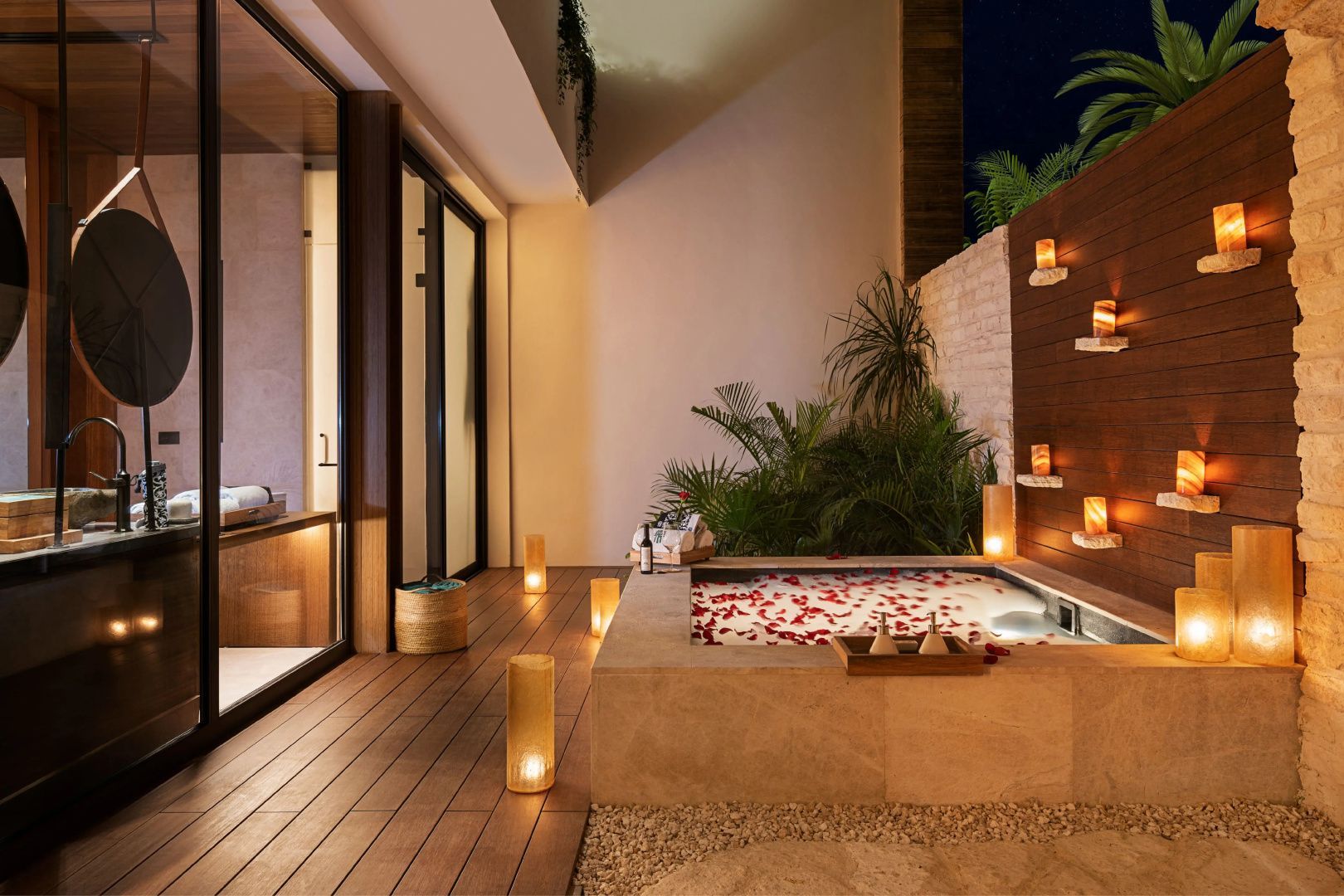Außenbadewanne mit Blütenblättern und Kerzenlicht auf einer Holzterrasse am Abend.