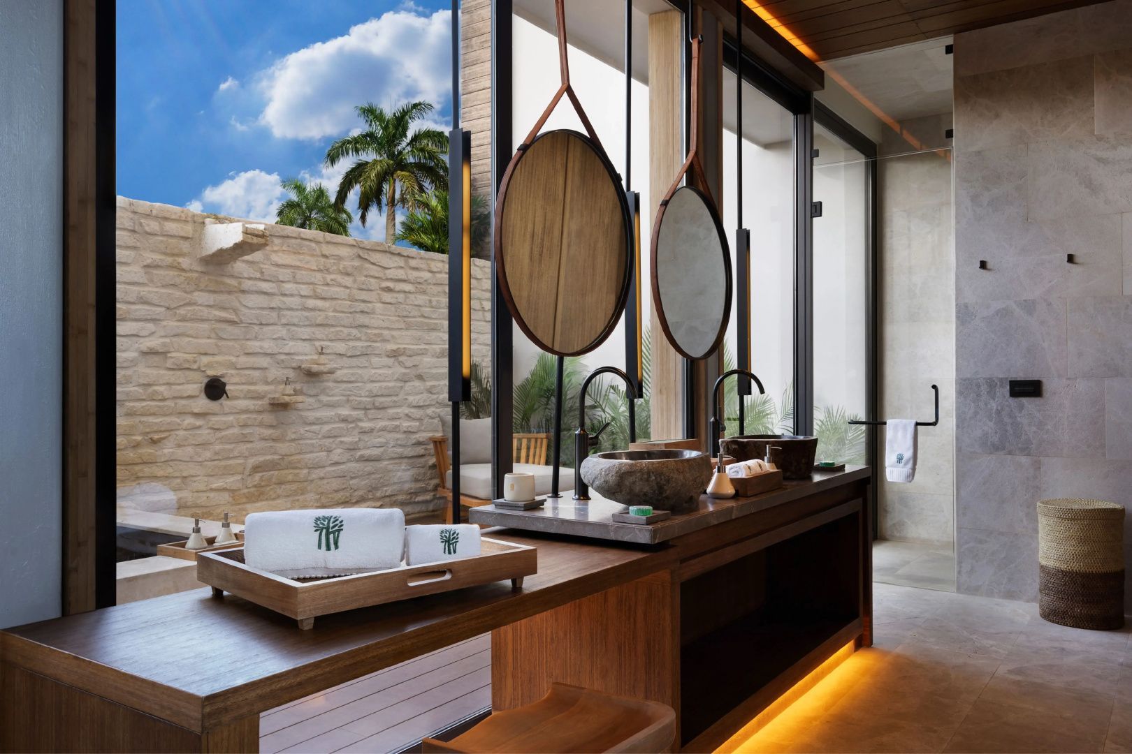 Badezimmer mit Doppelwaschtisch aus Stein, rundem Spiegel und Blick in den Innenhof.