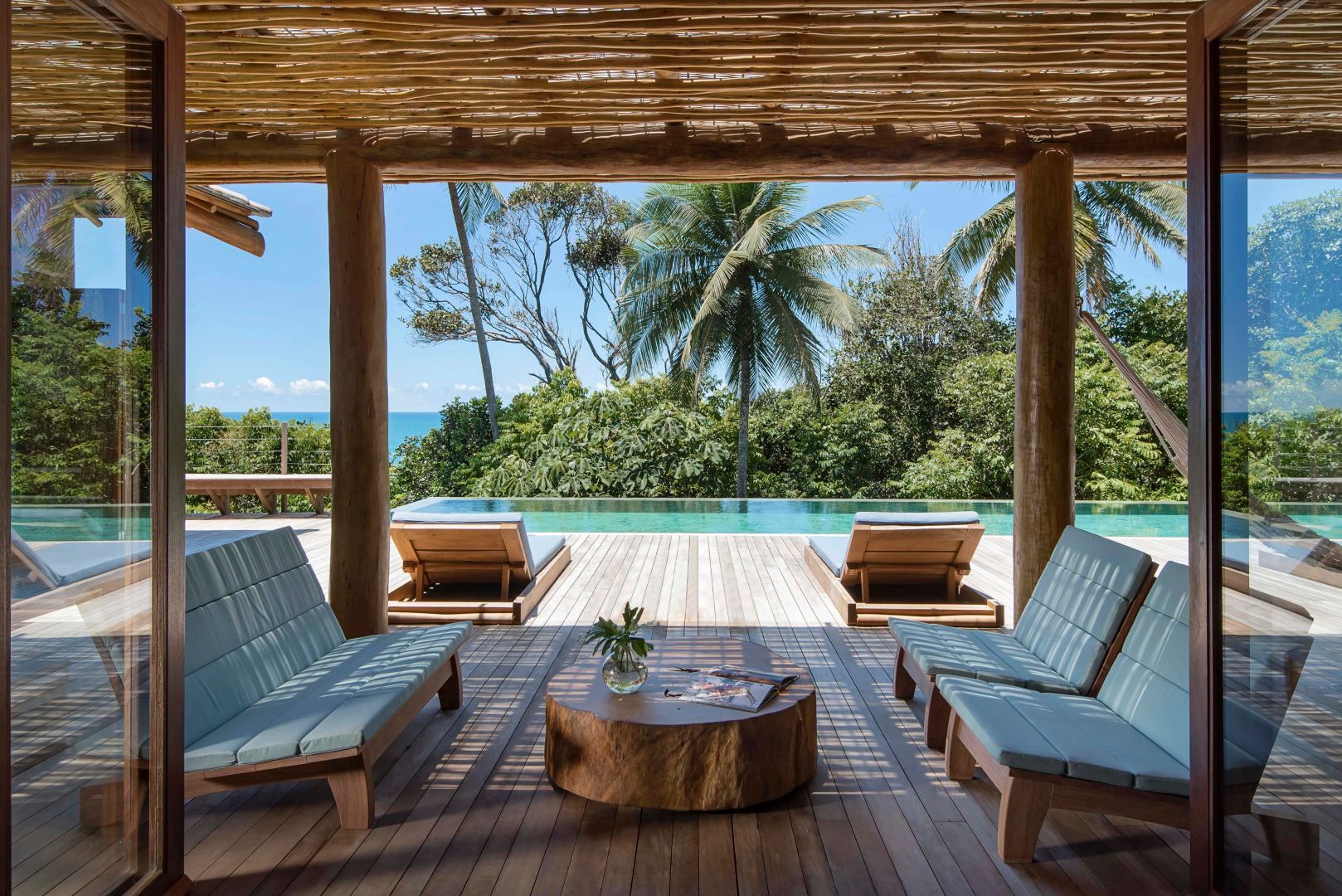 Überdachter Loungebereich aus Holz mit Blick auf den Pool und Palmen.