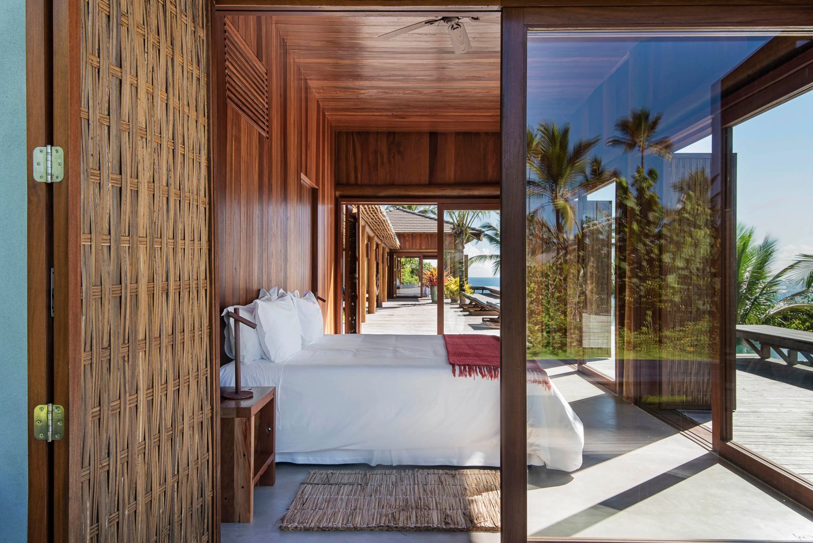 Blick durch eine Glasfront in ein Schlafzimmer mit Holzverkleidung und weißem Bett.