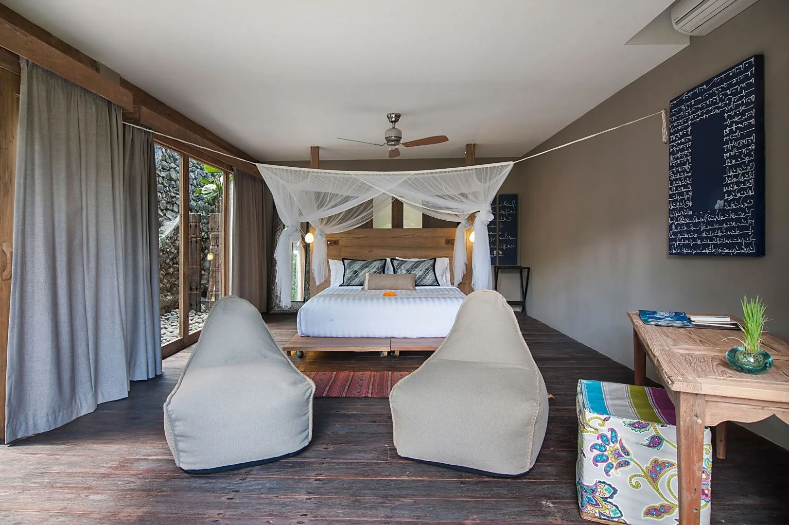 Geräumiges Zimmer mit Doppelbett, Mückennetz, Sitzsäcken und Holzboden.