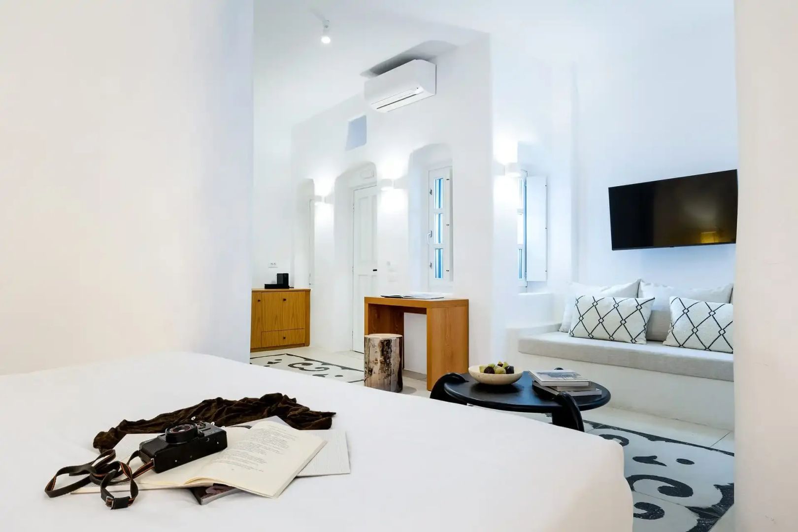 Weiß eingerichtetes Hotelzimmer mit Doppelbett, Sitzbereich und Holzmöbeln.