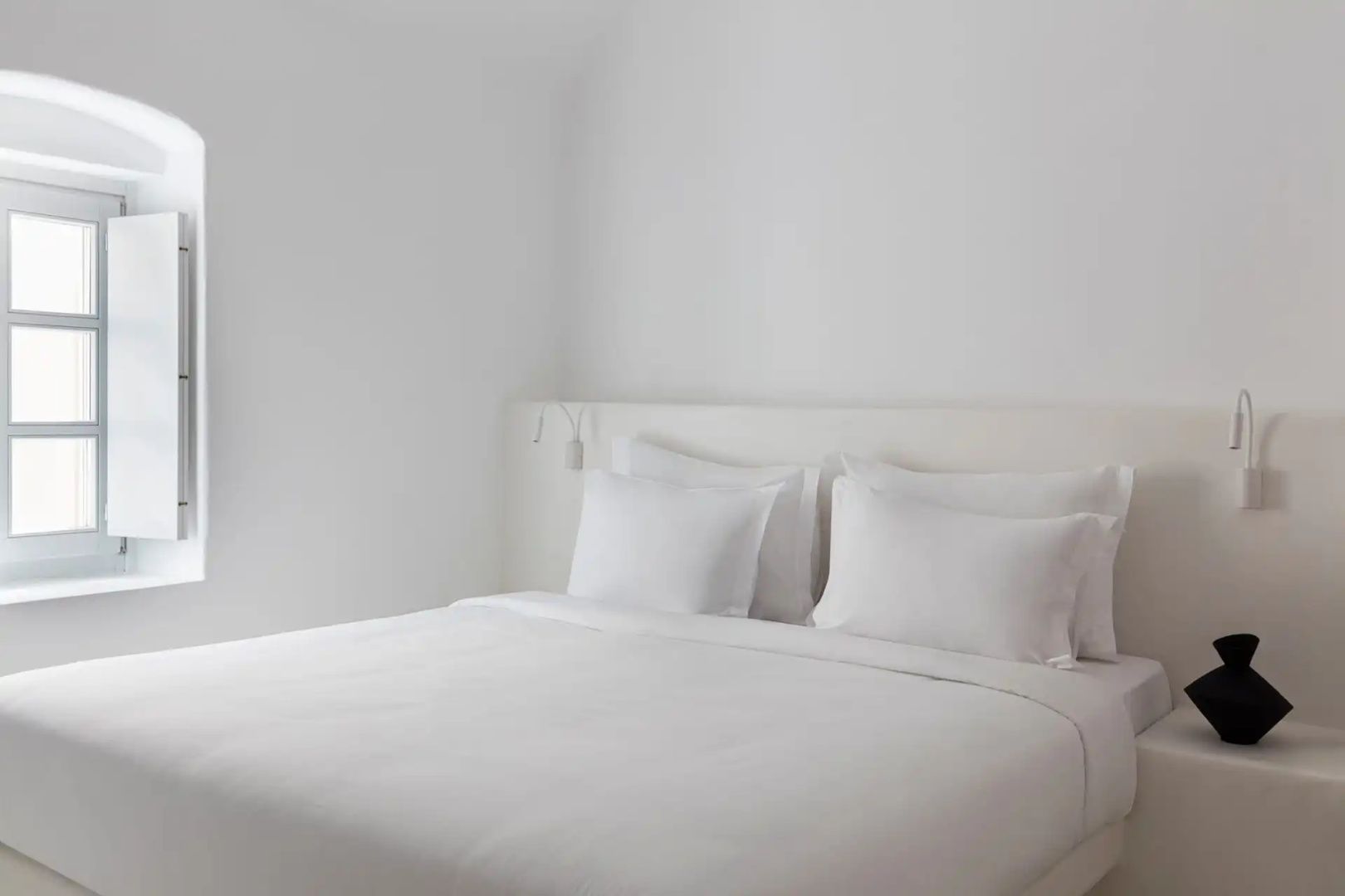 Doppelbett mit weißer Bettwäsche und Kissen in einem schlichten weißen Raum