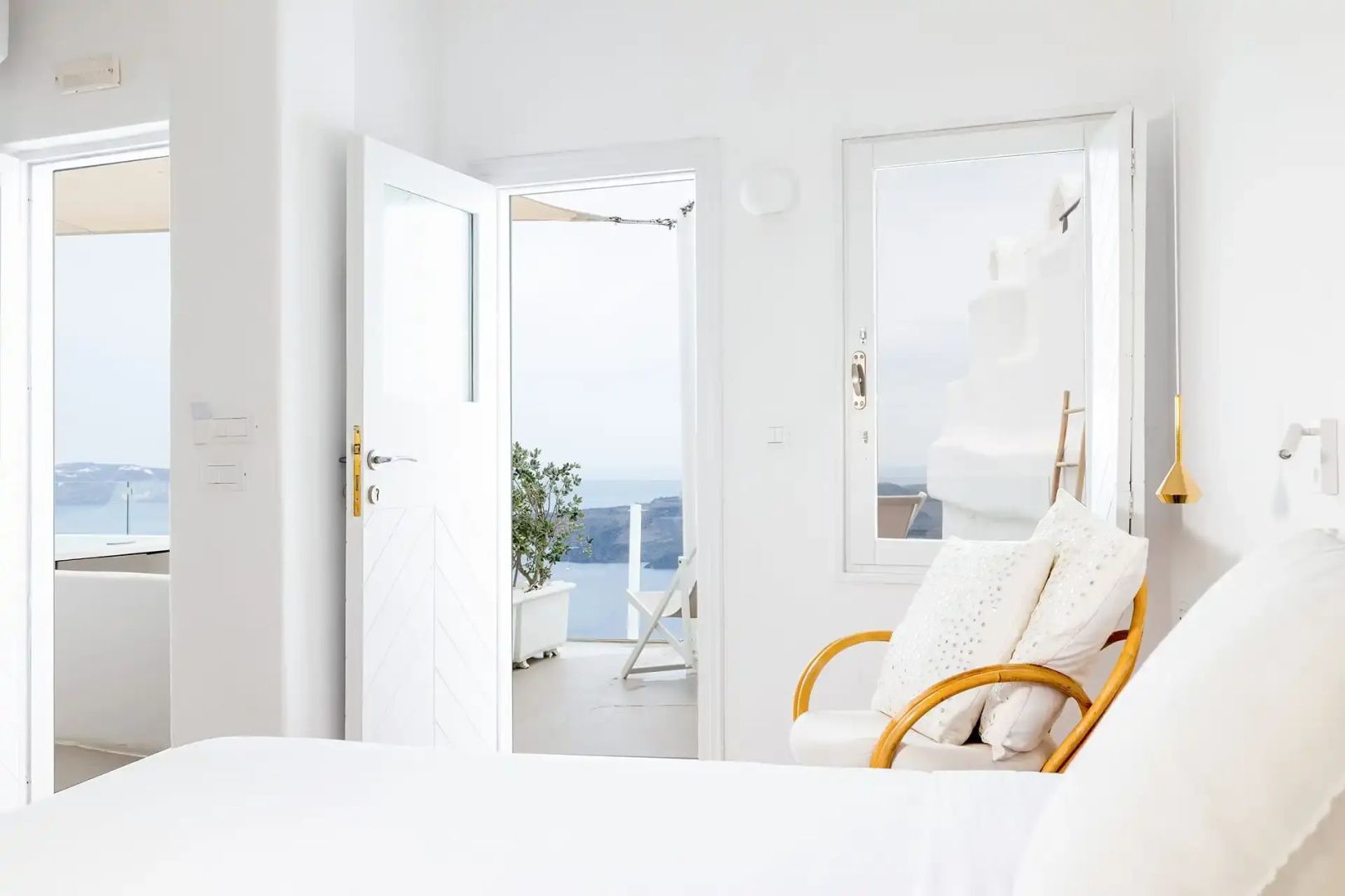 Helles Hotelzimmer mit Sessel und geöffnete Tür zur Terrasse mit Blick auf das Meer.