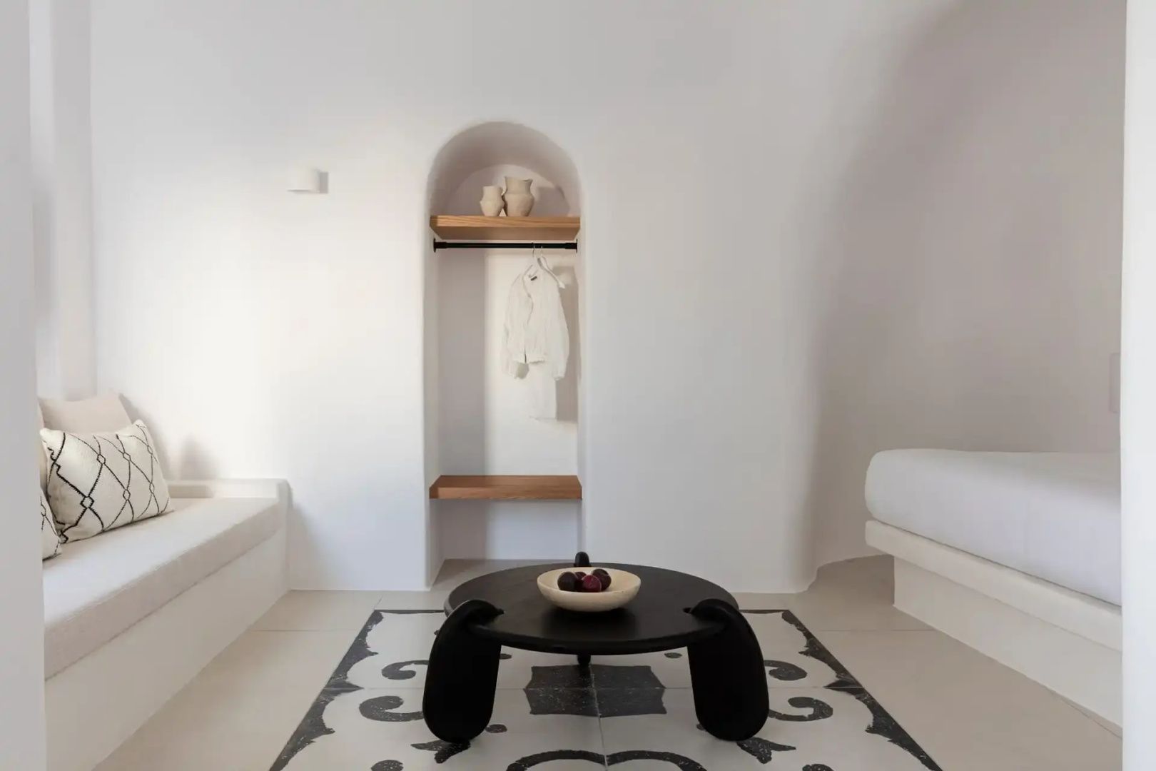 Heller Wohnbereich mit weiß geschwungener Wand, dunklem Couchtisch und Mosaikboden.