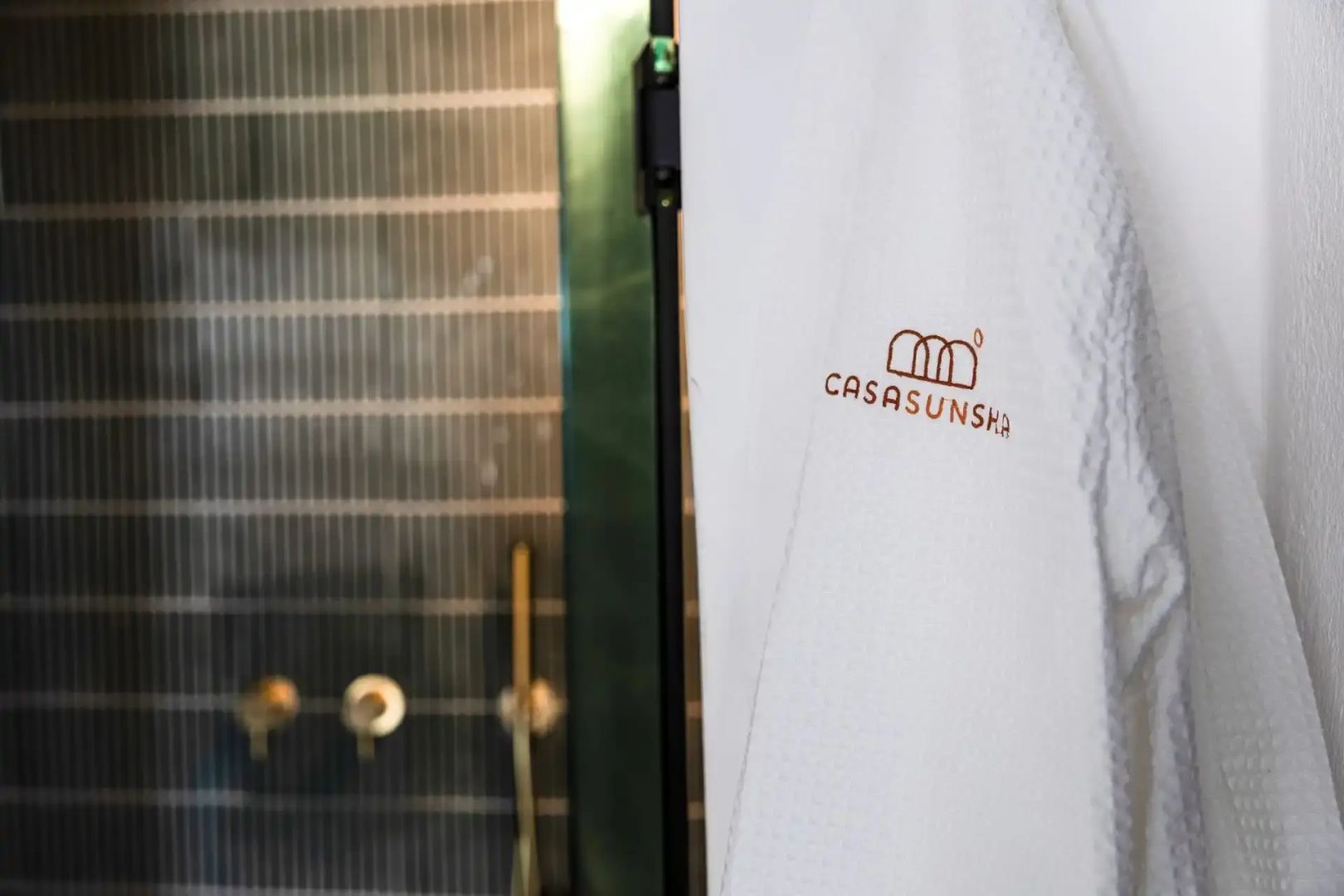 Weißer Bademantel mit Hotelaufschrift vor einer dunkel gefliesten Dusche