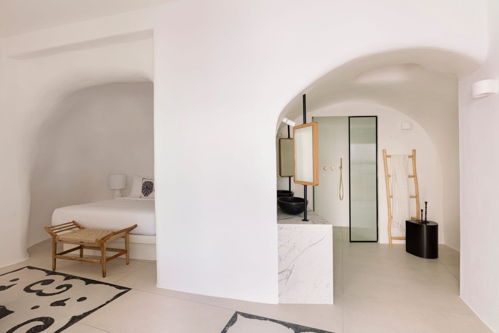 Offenes Hotelzimmer mit weißer Bogenarchitektur, Bettbereich und modernem Waschtisch.