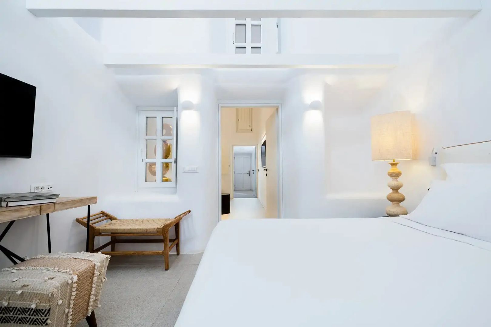 Weiß gestaltetes Schlafzimmer mit Holzbank, Stehlampe und Blick in den Flur.