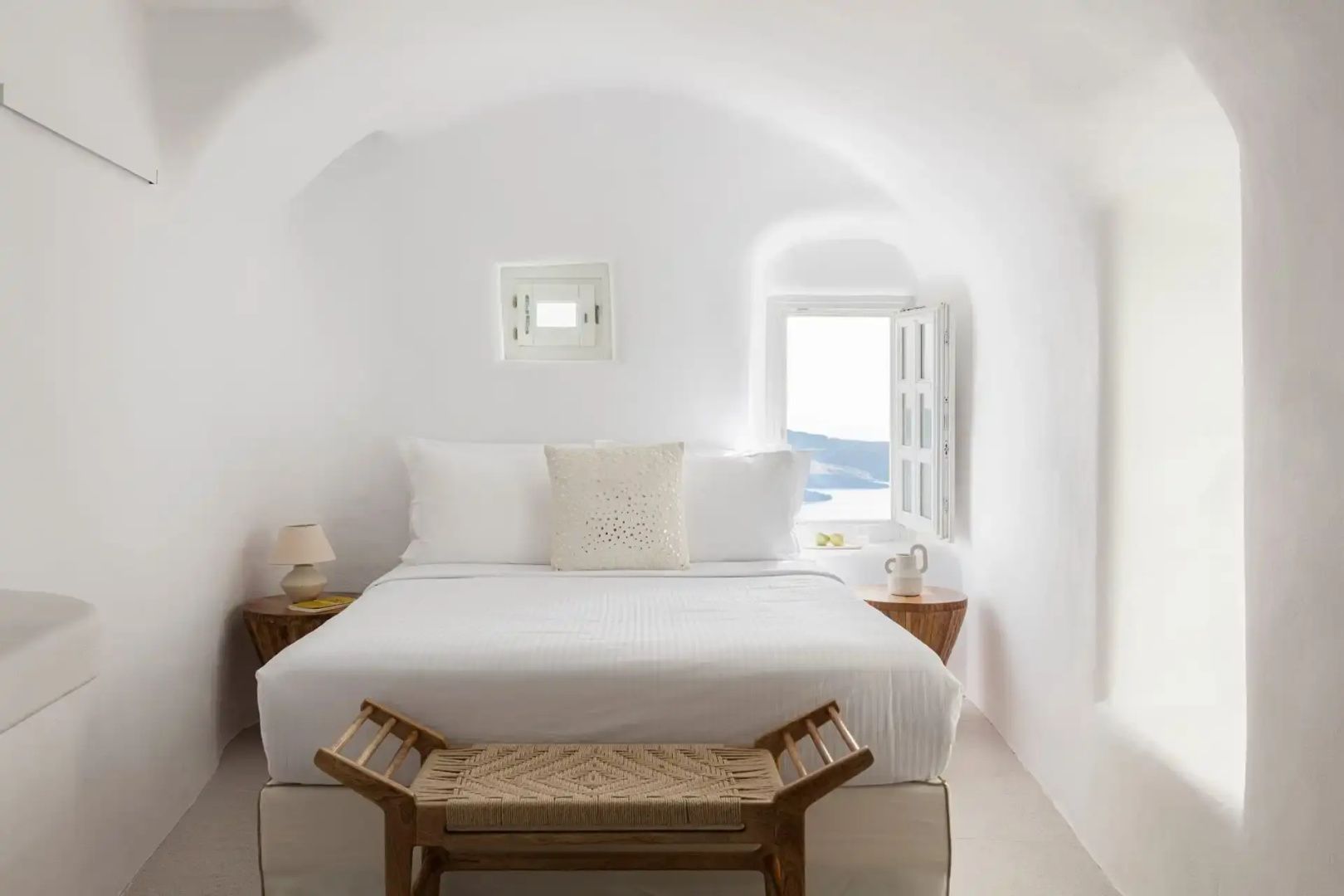 Weißes Schlafzimmer in Gewölbeform mit Doppelbett, Sitzbank und Fenster mit Blick aufs Meer.