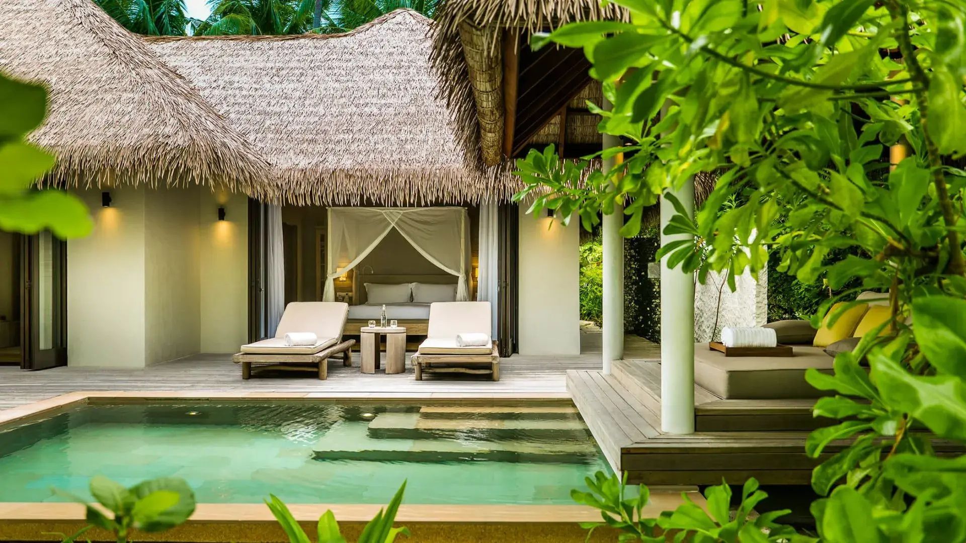 Sonnendeck einer Reetdachvilla mit kleinem Pool, zwei Sonnenliegen und Blick zum Bett.