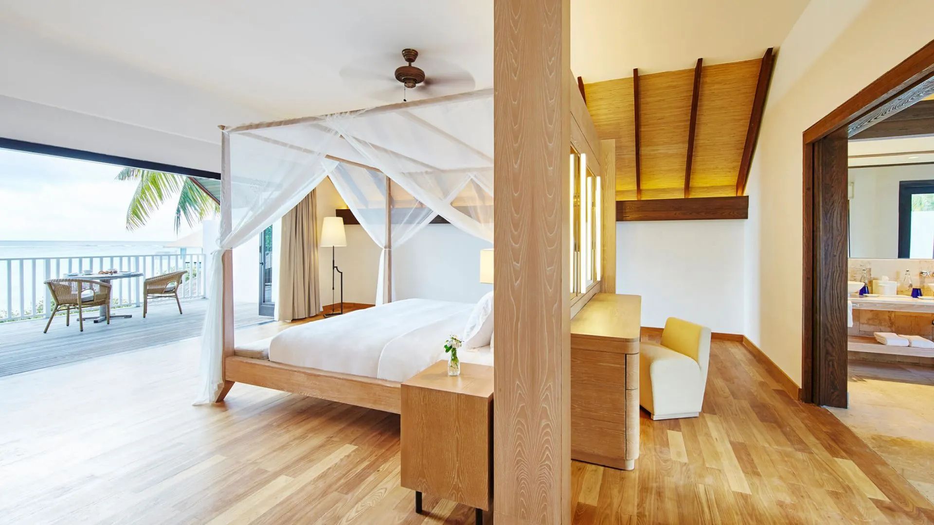 Helles Schlafzimmer mit einem Himmelbett aus Holz, Moskitonetz und Holzmöbeln.