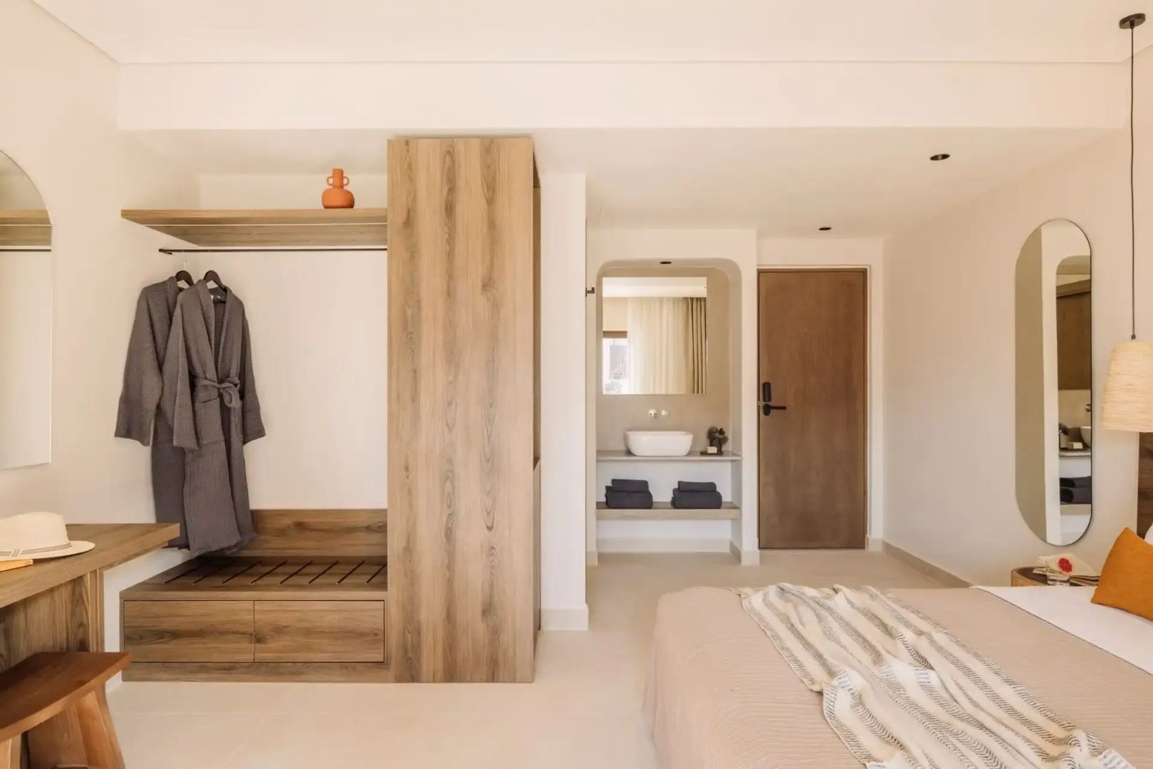 Hell eingerichtetes Zimmer mit Holzschrank, Bademantel und Waschnische im Hintergrund.