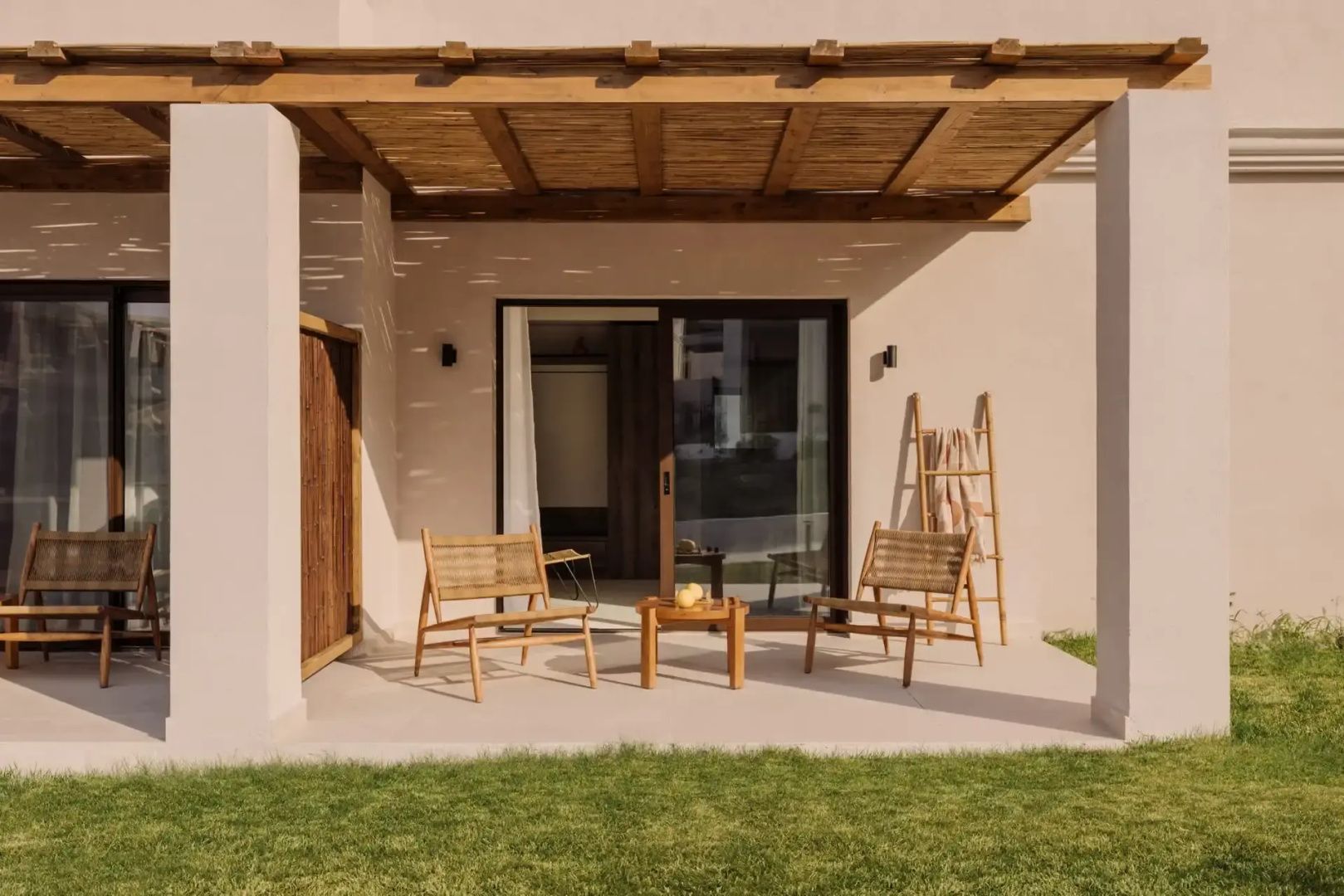 Überdachte Terrasse mit zwei Holzstühlen, einem kleinen Tisch und direktem Zugang zum Rasen.