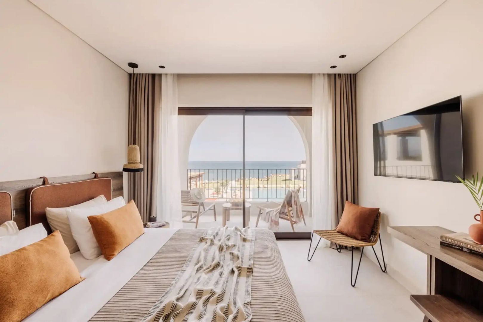Hotelzimmer mit Doppelbett, Sitzgelegenheit und Balkon mit Ausblick auf das Meer.