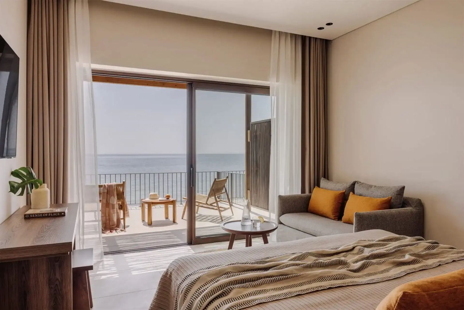 Hotelzimmer mit Doppelbett, Sofa und geöffneter Balkontür mit Blick auf das Meer.