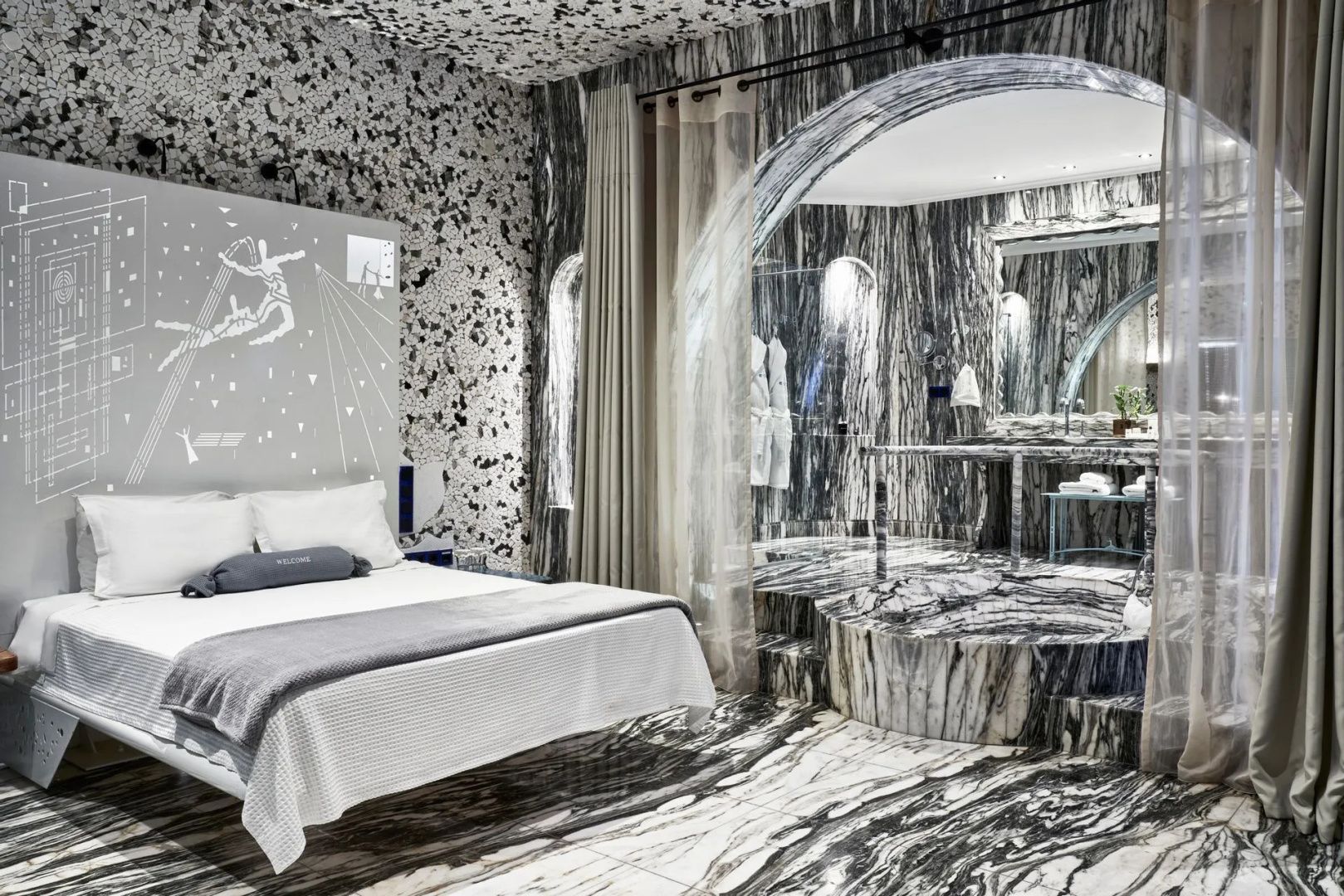 Hotelzimmer mit gemustertem Marmorboden, Terrazzowänden und Blick auf das angrenzende Bad.