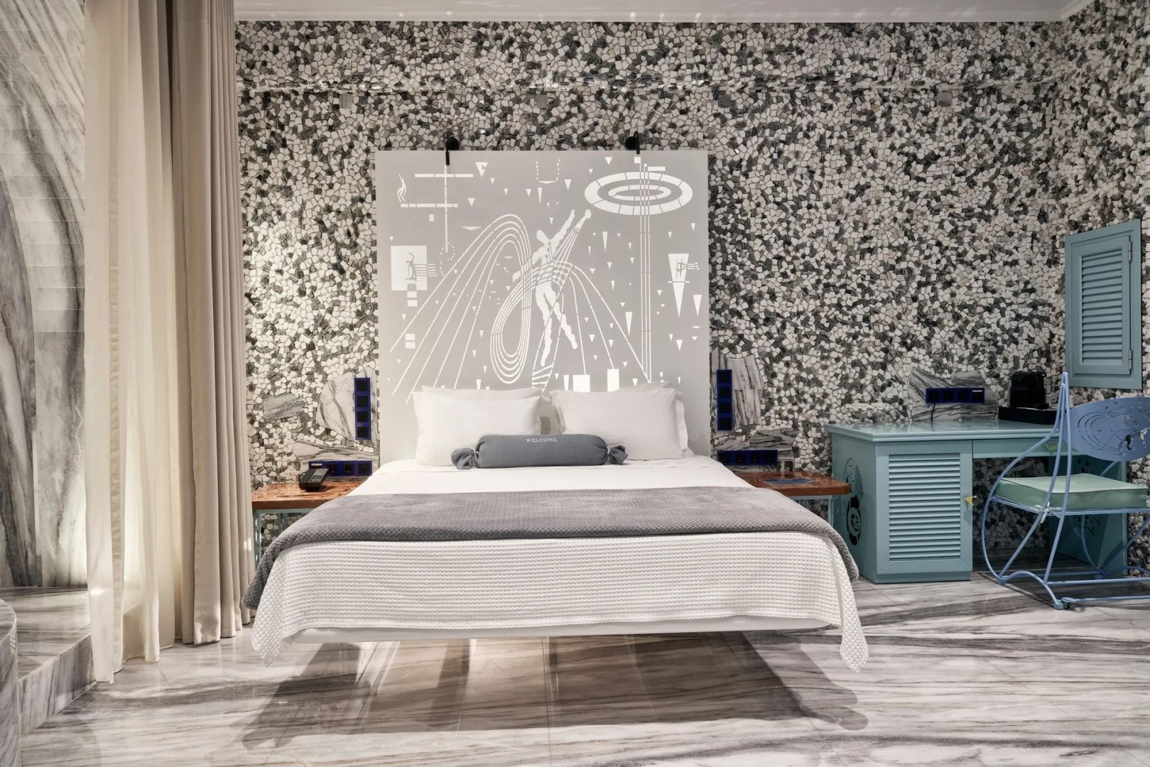 Doppelbett vor einer Mosaikwand mit weißem Kopfteil und feinen Zeichnungen.