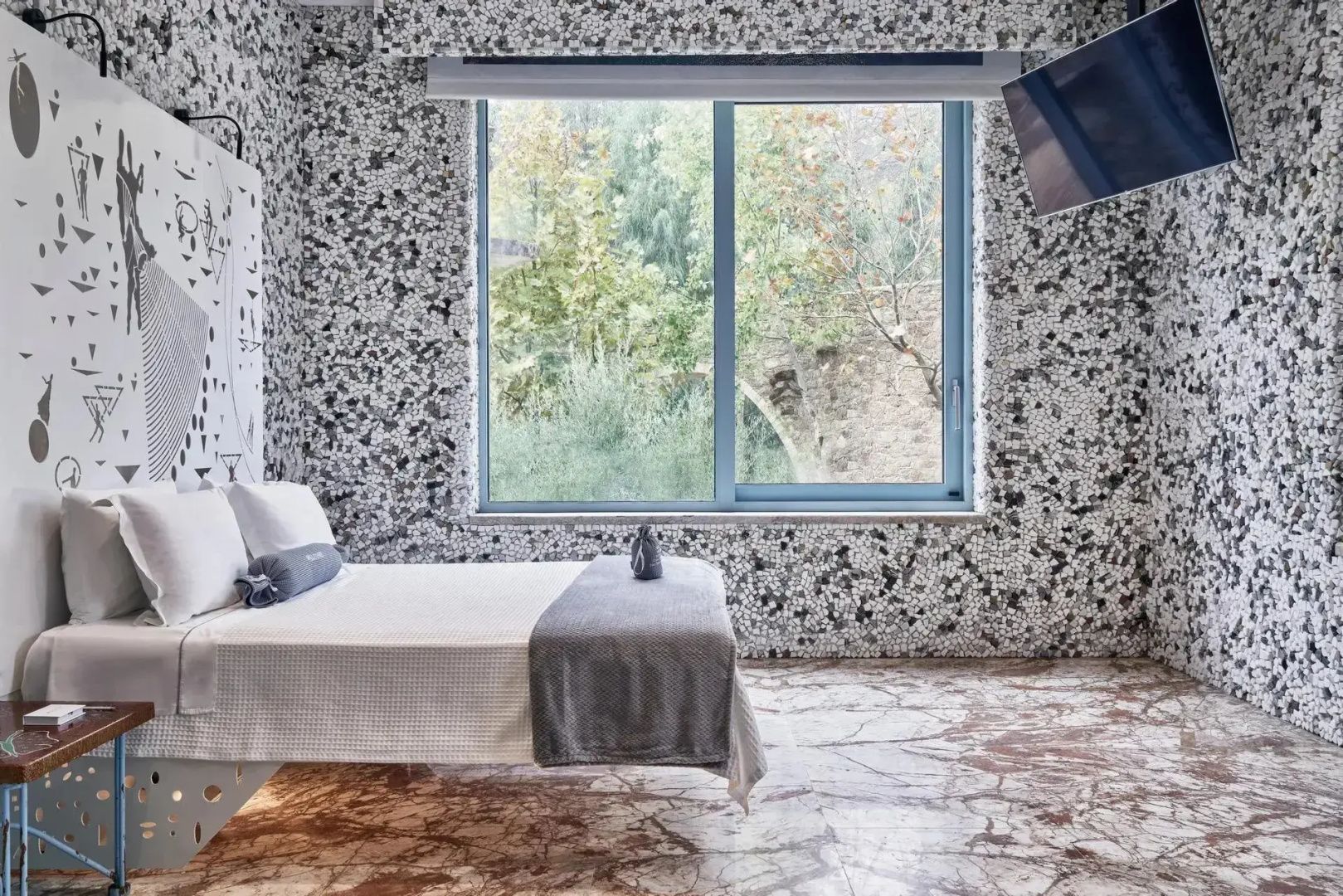 Schlafzimmer mit gemusterter Mosaikwand, großem Bett und Blick ins Grüne.