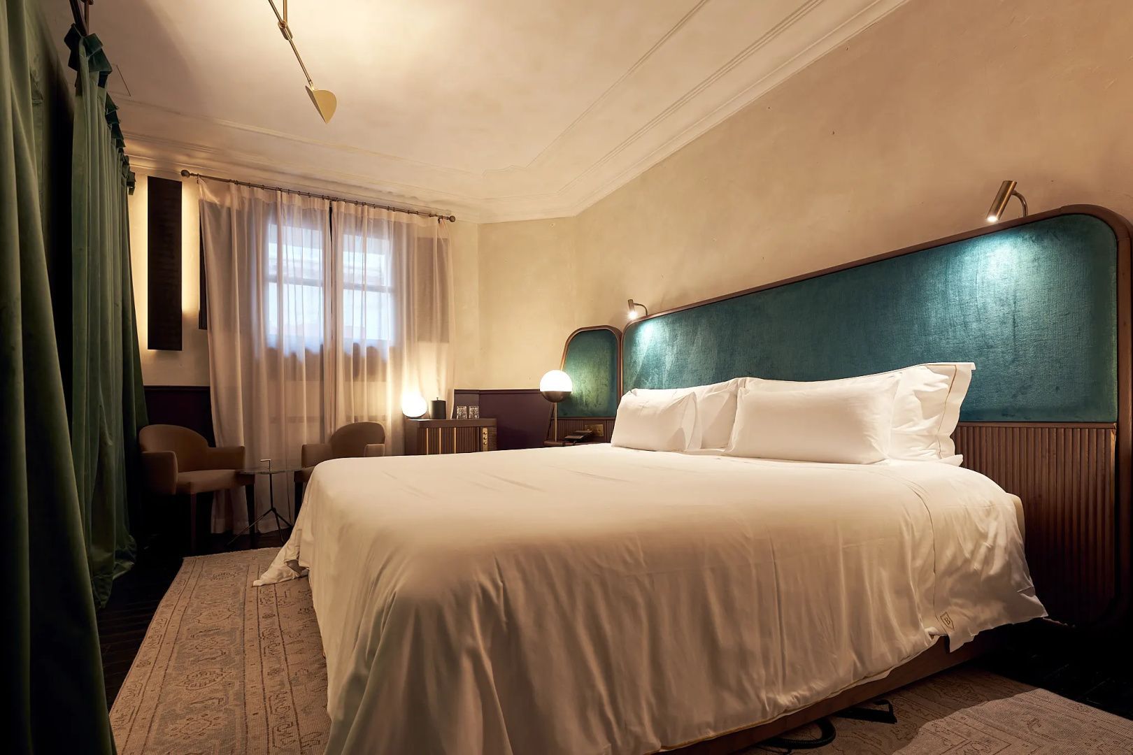 Doppelbett mit weißer Bettwäsche und grünem Kopfteil vor heller Wand im Hotelzimmer.