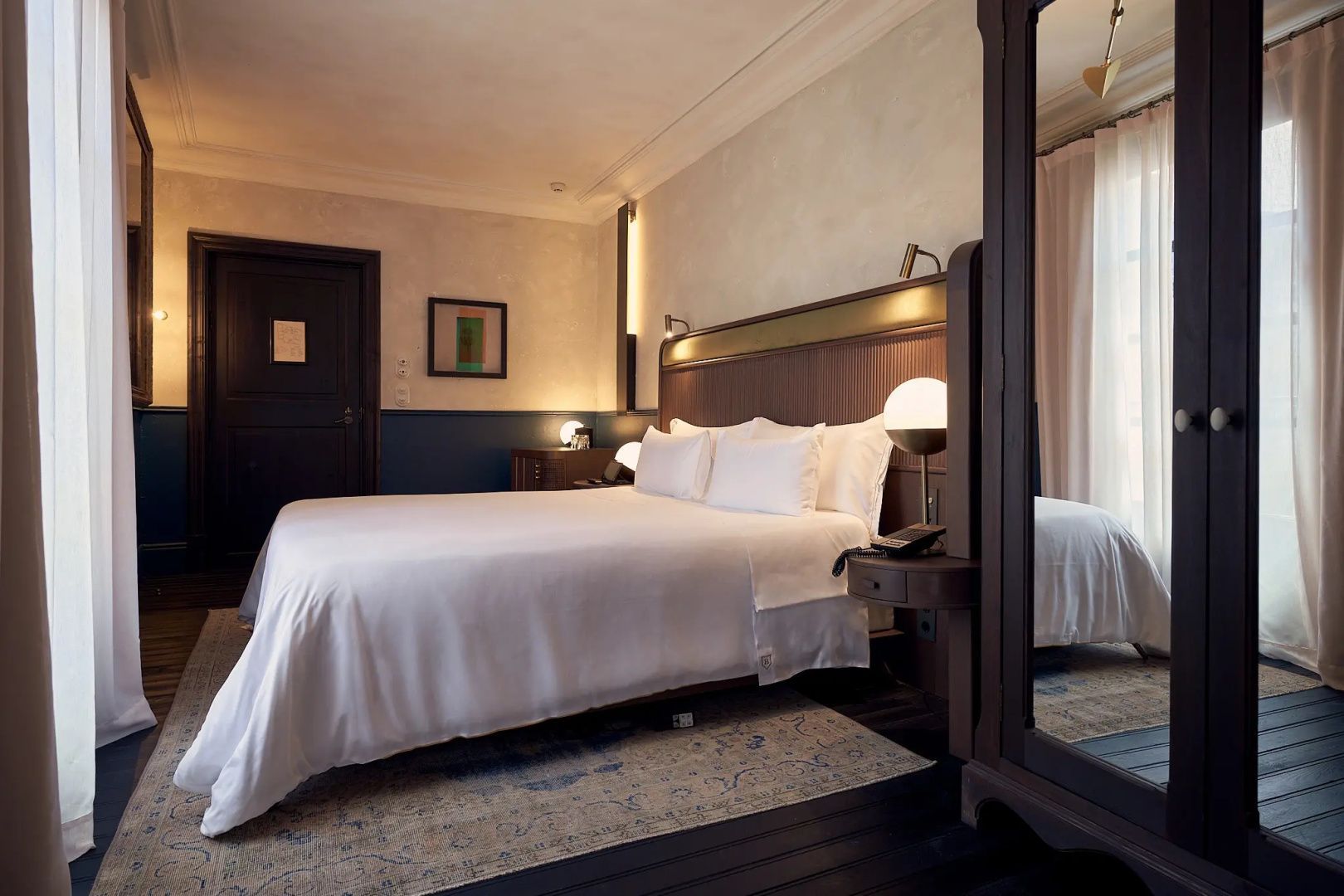 Großes Doppelbett mit weißem Bezug, hölzernes Kopfteil und Spiegel im Hotelzimmer.