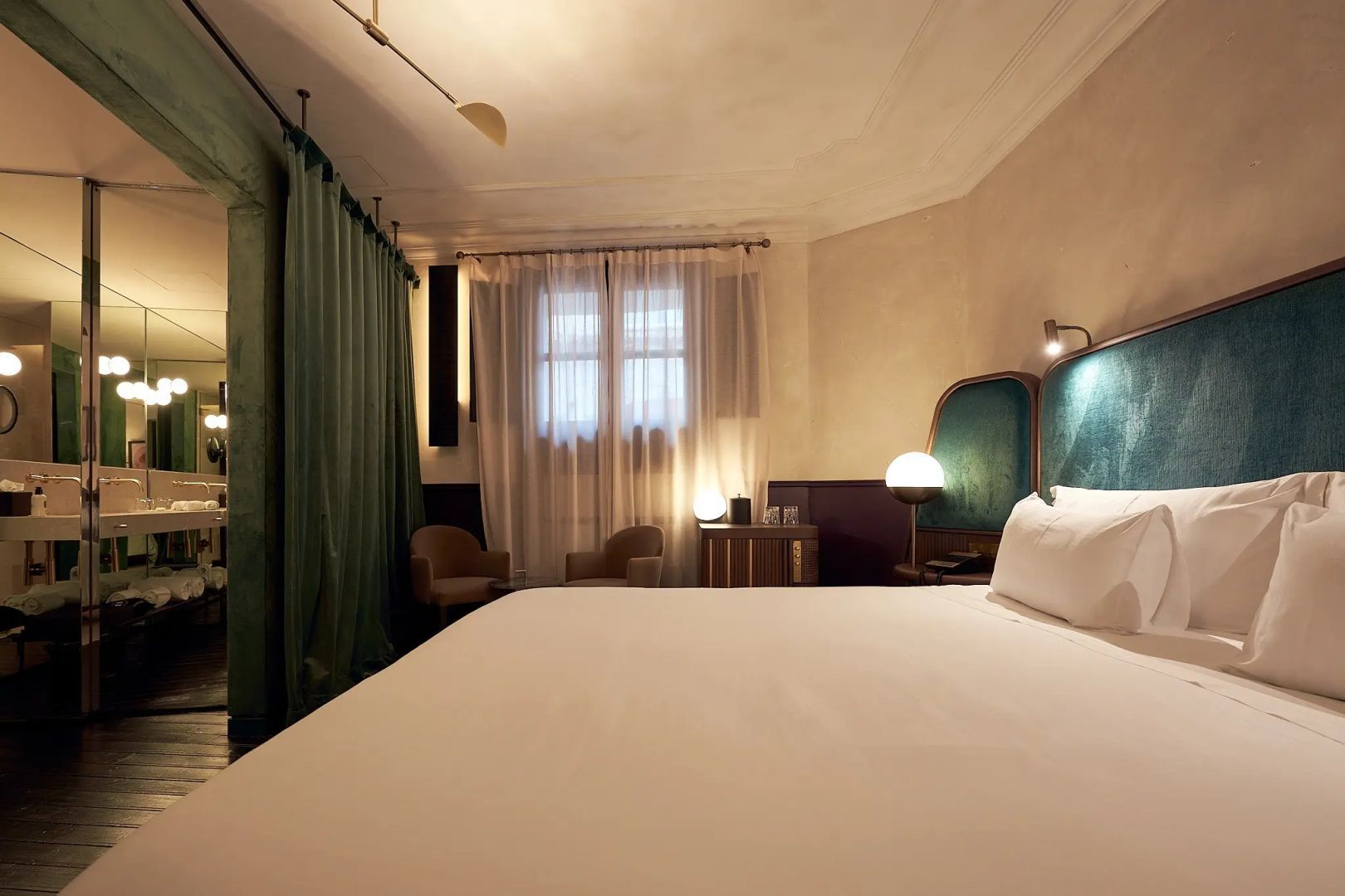 Hotelzimmer mit großem Doppelbett, grüner Vorhangdekoration und beleuchtetem Fenster.