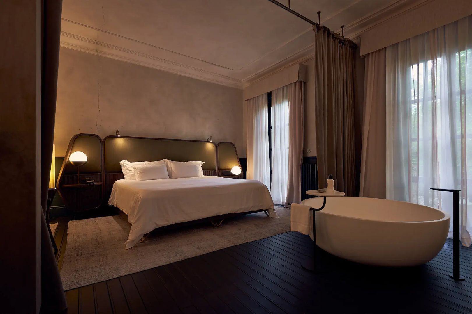 Hotelzimmer mit großem Doppelbett, dunklem Holzboden und freistehender Badewanne.
