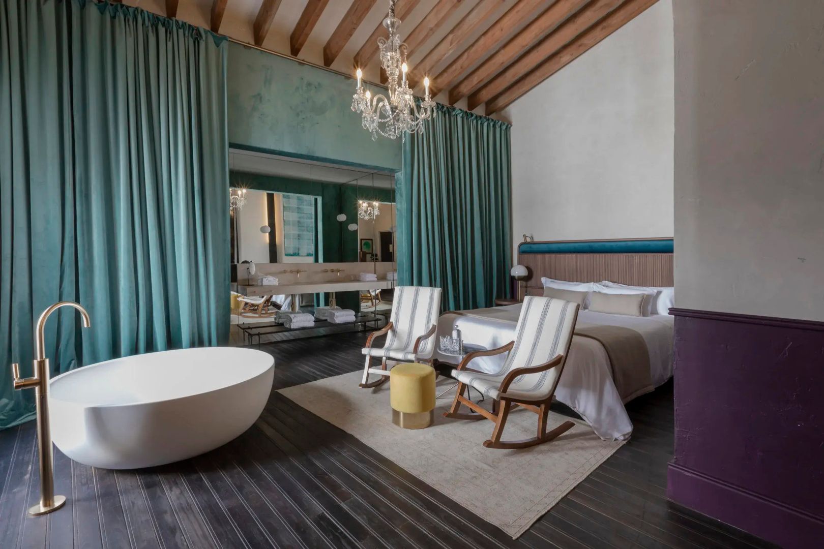 Großes Hotelzimmer mit Holzbalkendecke, Schaukelstühlen und freistehender Badewanne.